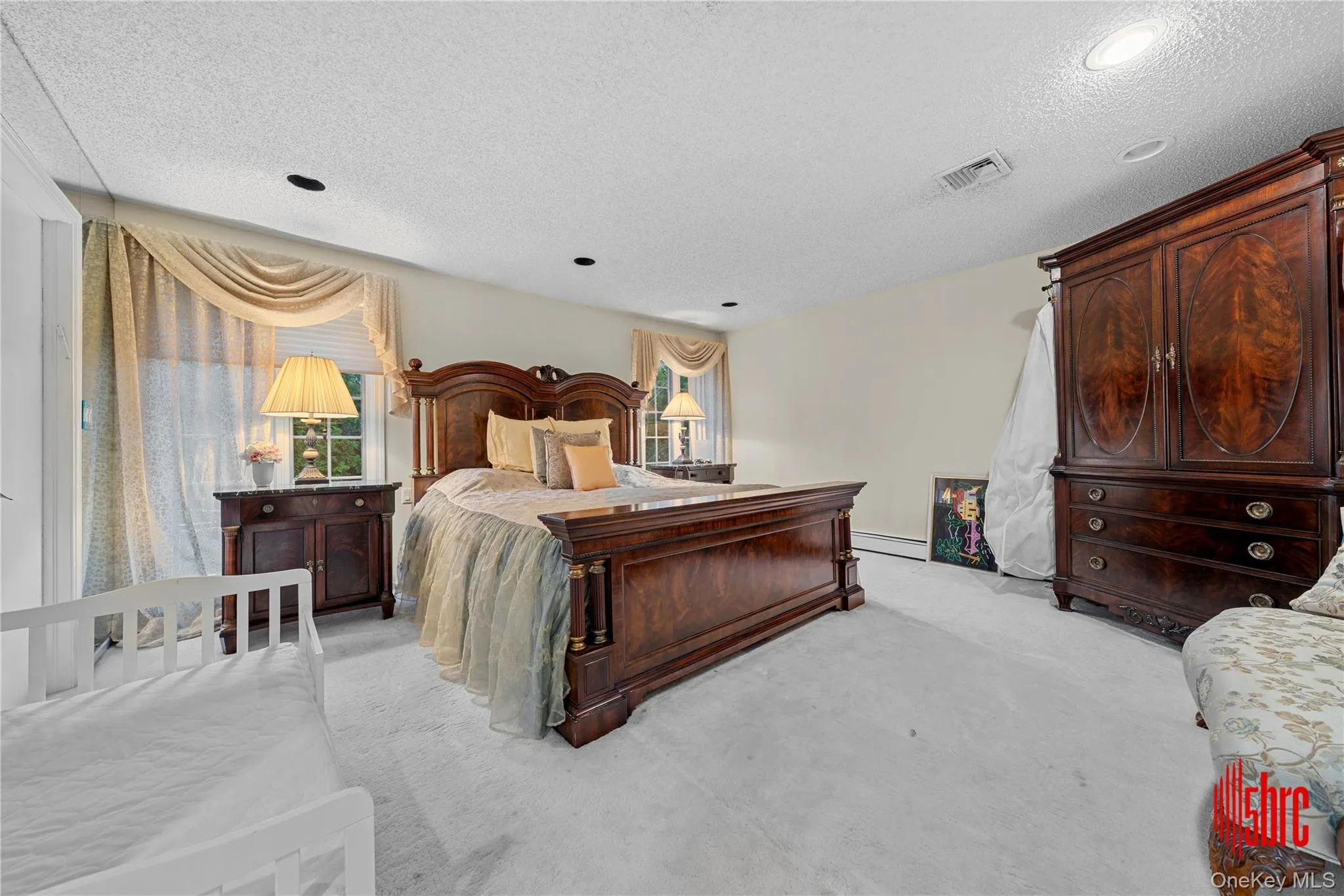 Bedroom featuring light colored carpet, a textured ceiling, and a baseboard heating unit Bedroom featuring light colored carpet, a textured ceiling, and a baseboard heating unit