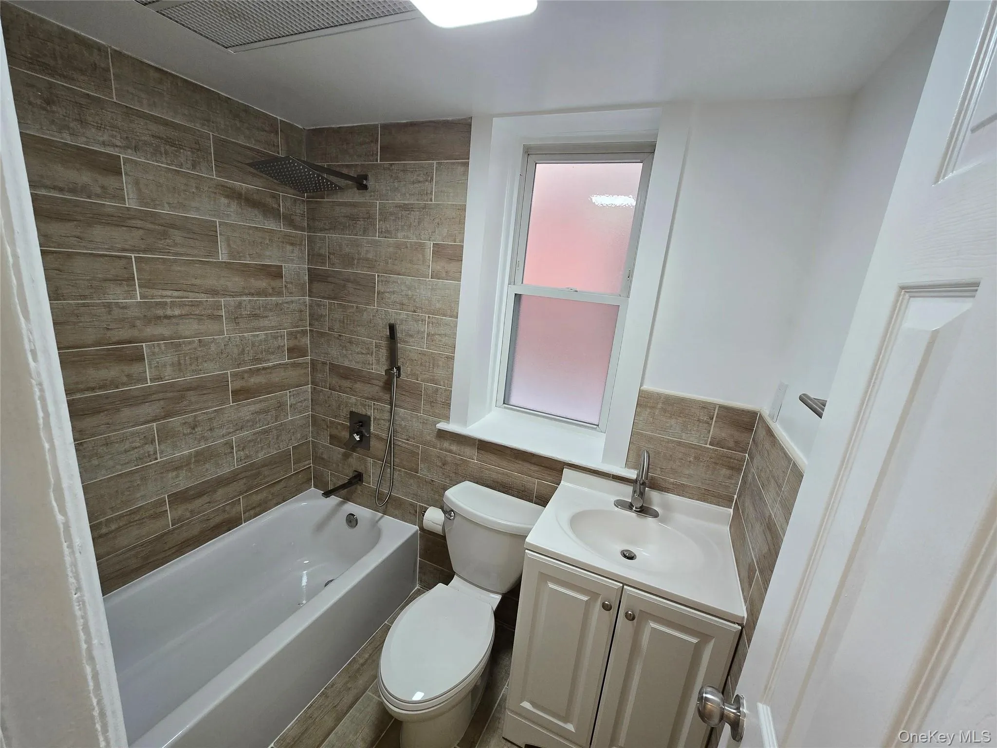 Full bath with vanity, tile walls, bathtub / shower combination, and wood tiled floors Full bath with vanity, tile walls, bathtub / shower combination, and wood tiled floors