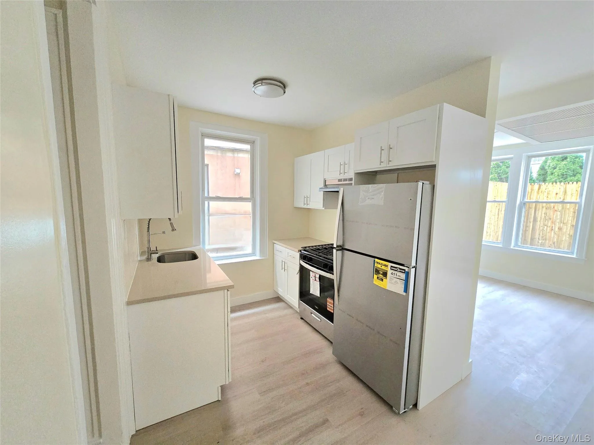 Kitchen featuring white cabinets, stainless steel appliances, light wood finished floors, light stone counters, and under cabinet range hood Kitchen featuring white cabinets, stainless steel appliances, light wood finished floors, light stone counters, and under cabinet range hood