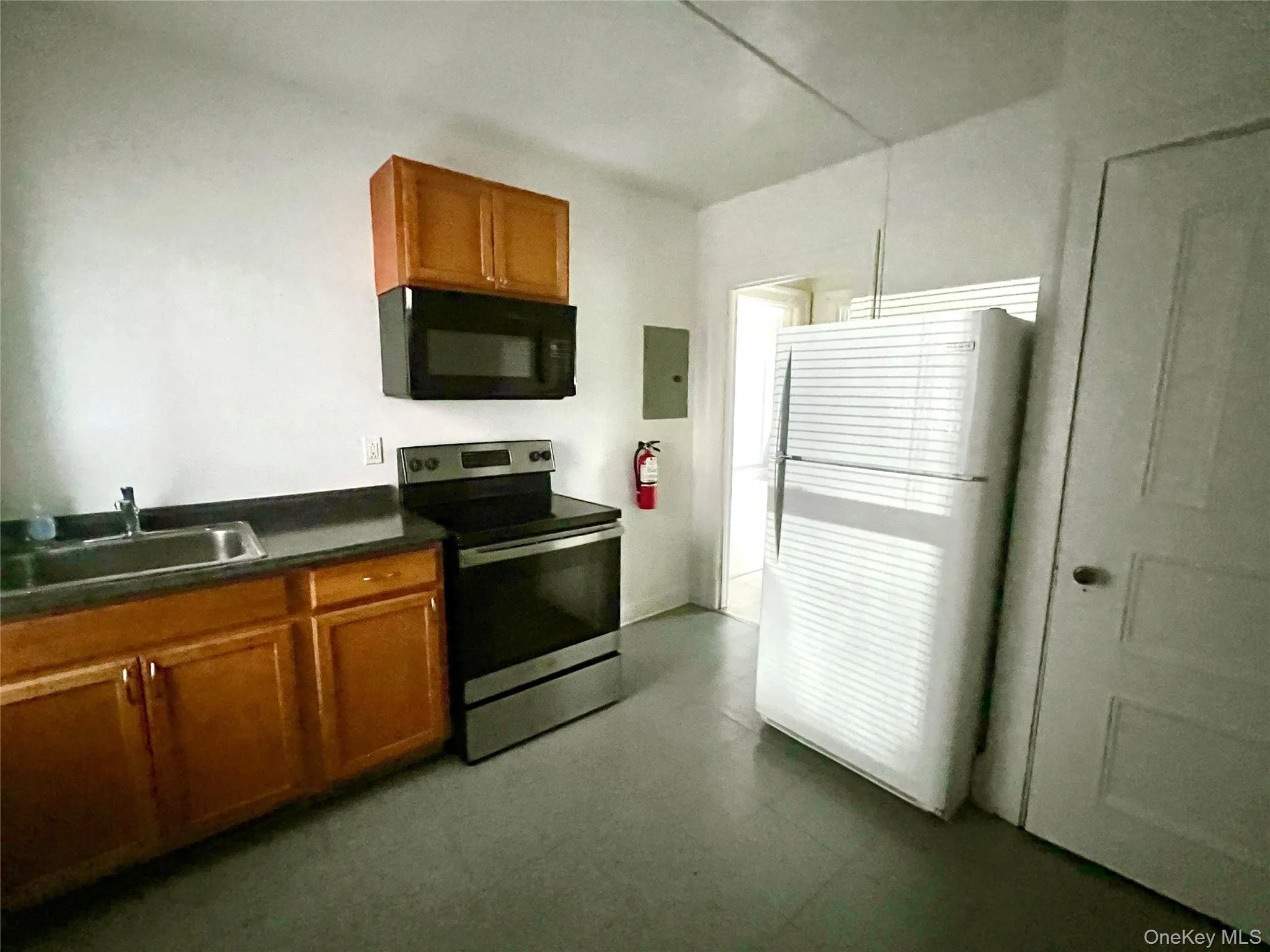 Kitchen with brown cabinetry, electric stove, dark countertops, and black microwave Kitchen with brown cabinetry, electric stove, dark countertops, and black microwave