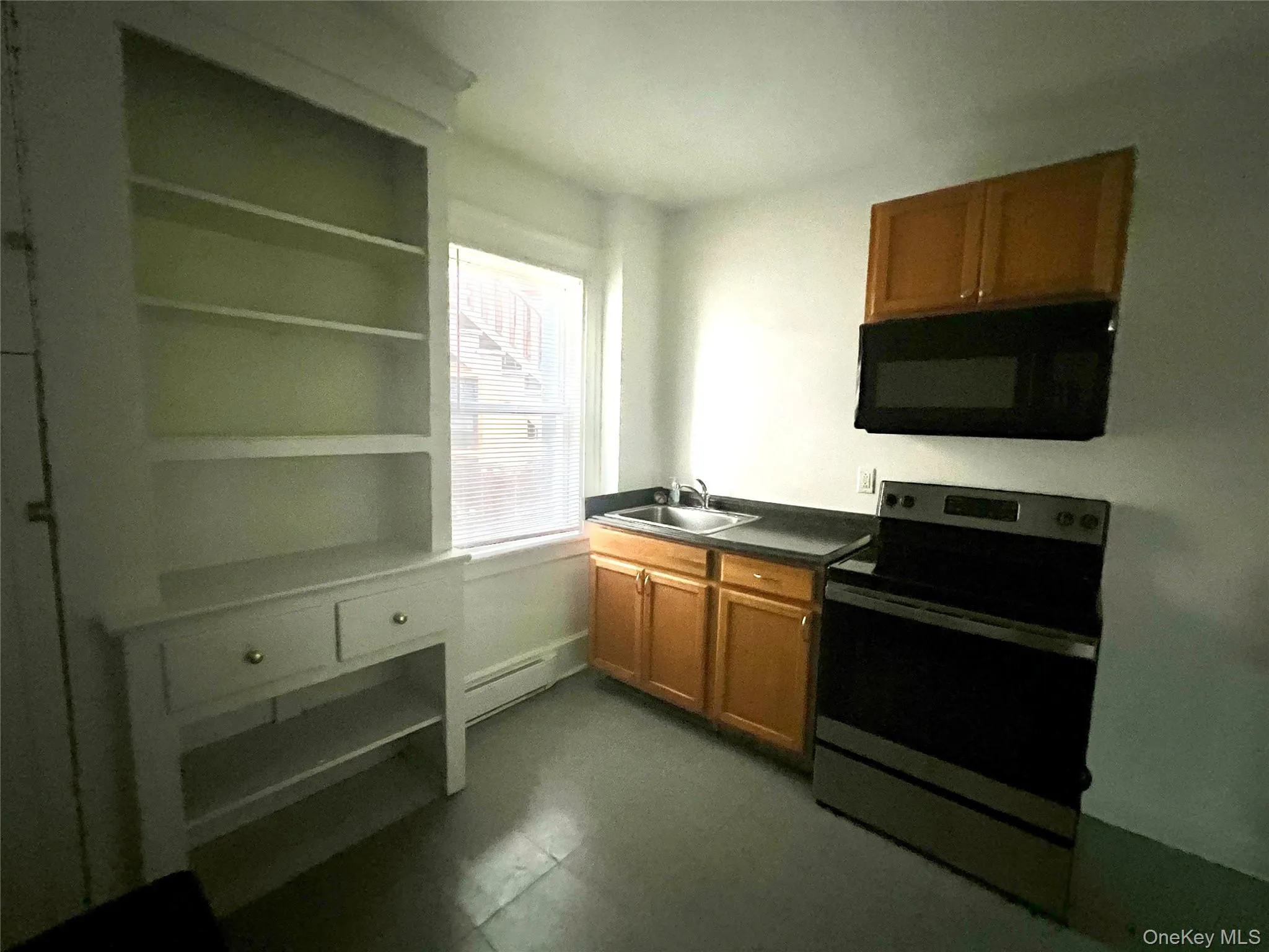 Kitchen with electric range, brown cabinets, black microwave, and dark countertops Kitchen with electric range, brown cabinets, black microwave, and dark countertops