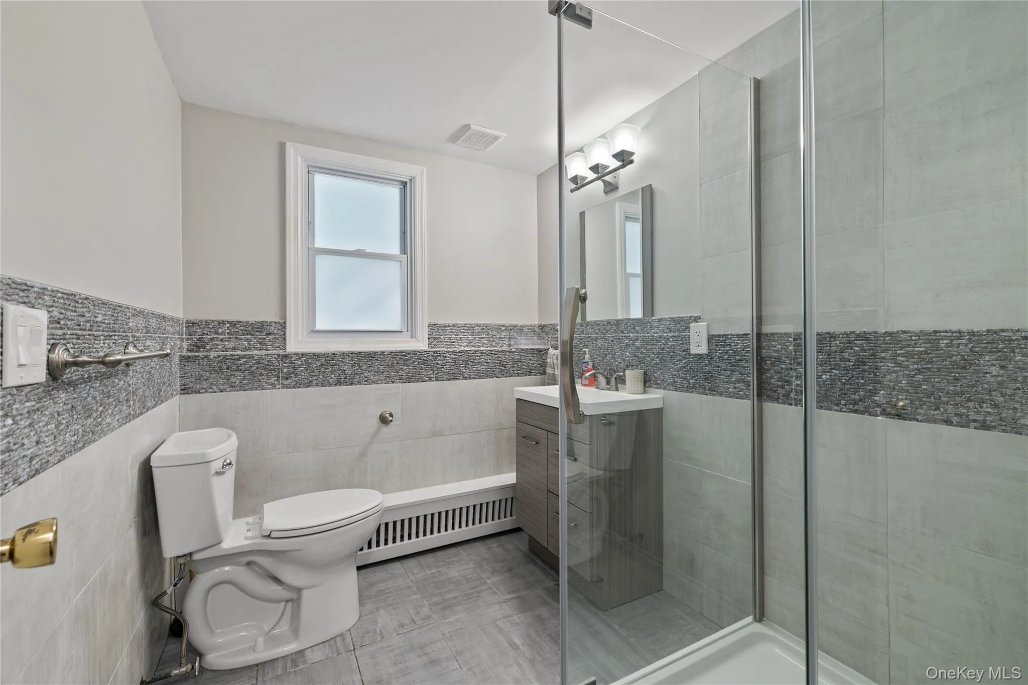 Bathroom featuring vanity, a stall shower, tile walls, radiator heating unit, and a wainscoted wall Bathroom featuring vanity, a stall shower, tile walls, radiator heating unit, and a wainscoted wall