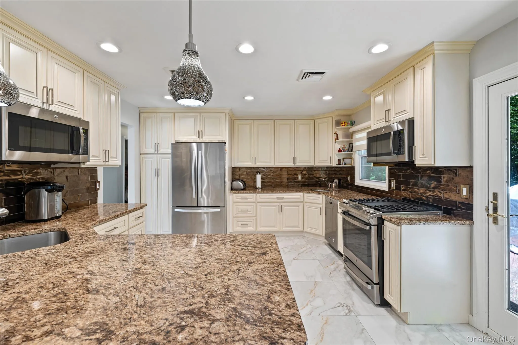 Kitchen with cream cabinetry, decorative backsplash, dark stone countertops, appliances with stainless steel finishes, and recessed lighting Kitchen with cream cabinetry, decorative backsplash, dark stone countertops, appliances with stainless steel finishes, and recessed lighting