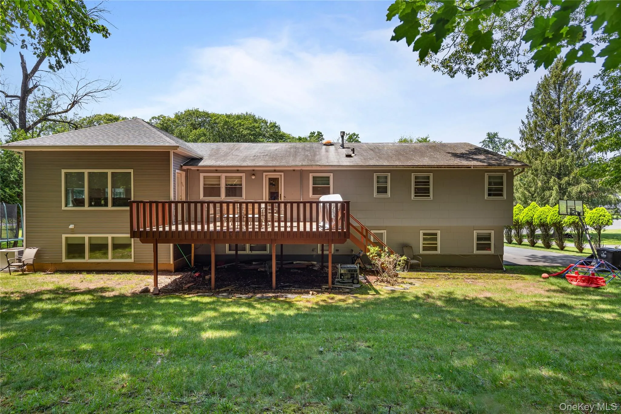 Rear view of property featuring a deck, a lawn, a shingled roof, and stairs Rear view of property featuring a deck, a lawn, a shingled roof, and stairs