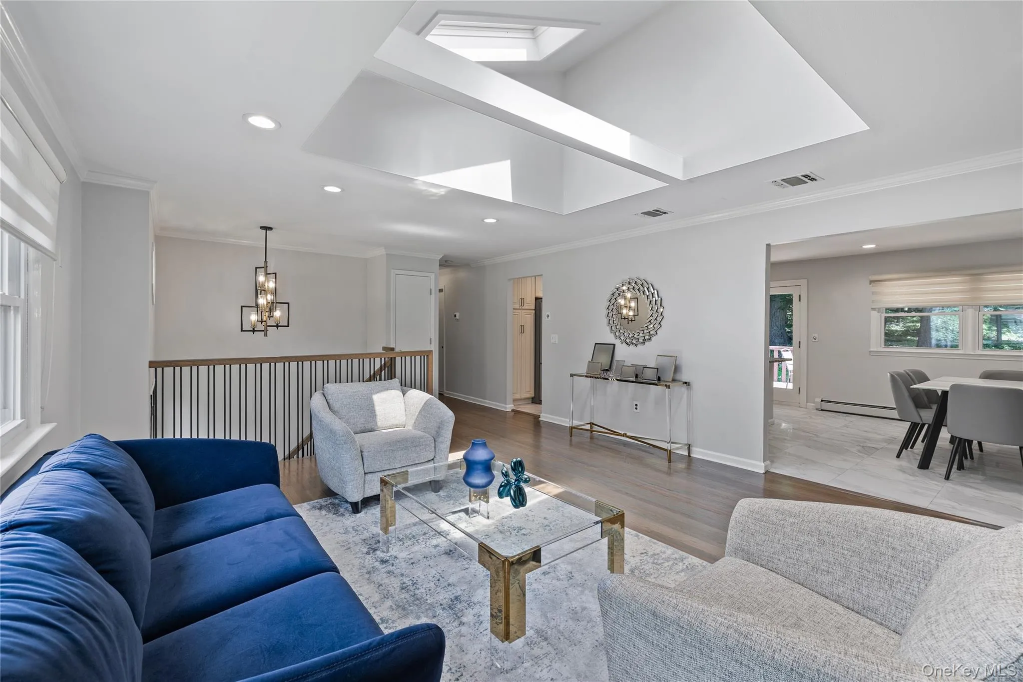 Living room with crown molding, recessed lighting, wood finished floors, a chandelier, and baseboard heating Living room with crown molding, recessed lighting, wood finished floors, a chandelier, and baseboard heating