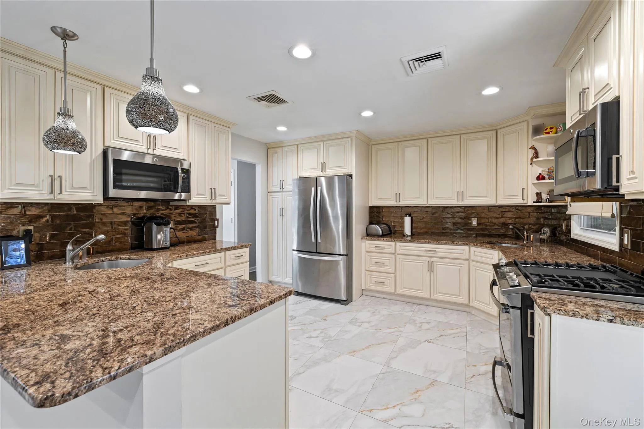 Kitchen with backsplash, cream cabinetry, stainless steel appliances, and recessed lighting Kitchen with backsplash, cream cabinetry, stainless steel appliances, and recessed lighting