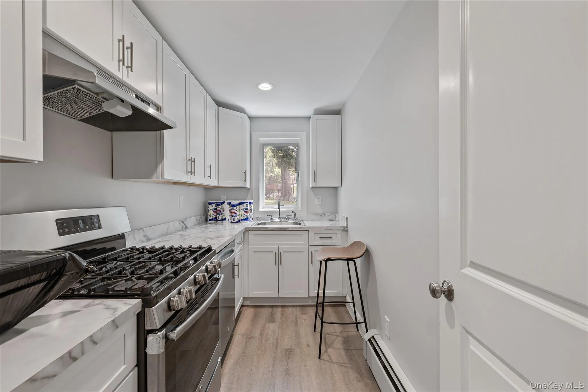 Kitchen featuring appliances with stainless steel finishes, light wood finished floors, white cabinets, a baseboard heating unit, and under cabinet range hood Kitchen featuring appliances with stainless steel finishes, light wood finished floors, white cabinets, a baseboard heating unit, and under cabinet range hood