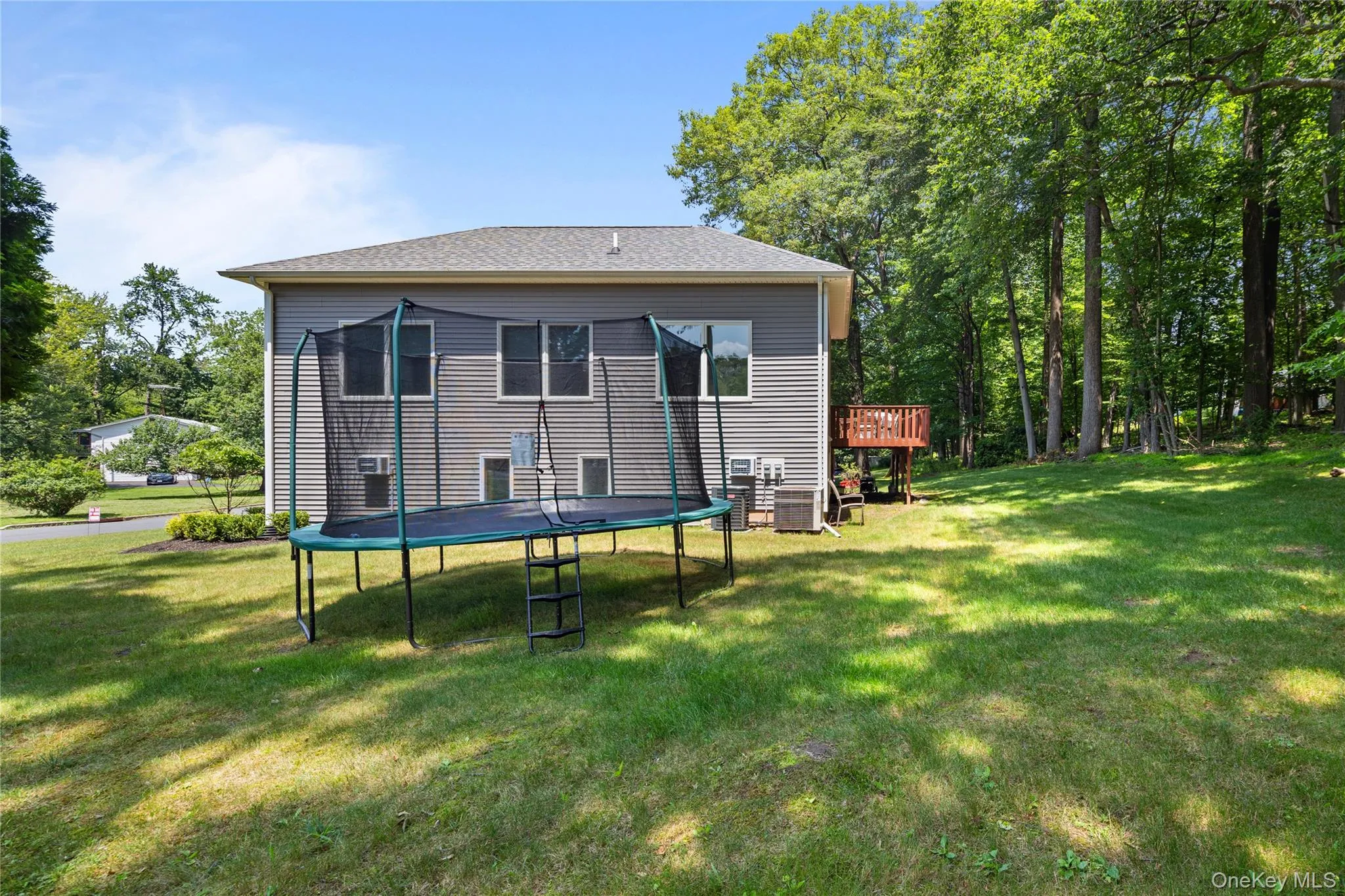 Rear view of property featuring a trampoline, a wooden deck, and a lawn Rear view of property featuring a trampoline, a wooden deck, and a lawn