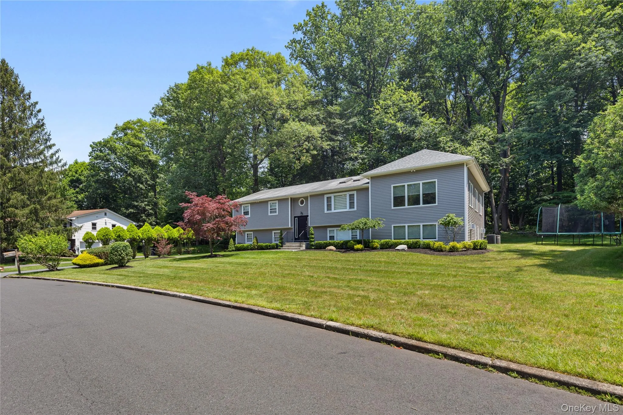 Bi-level home with a trampoline, view of scattered trees, and a front lawn Bi-level home with a trampoline, view of scattered trees, and a front lawn