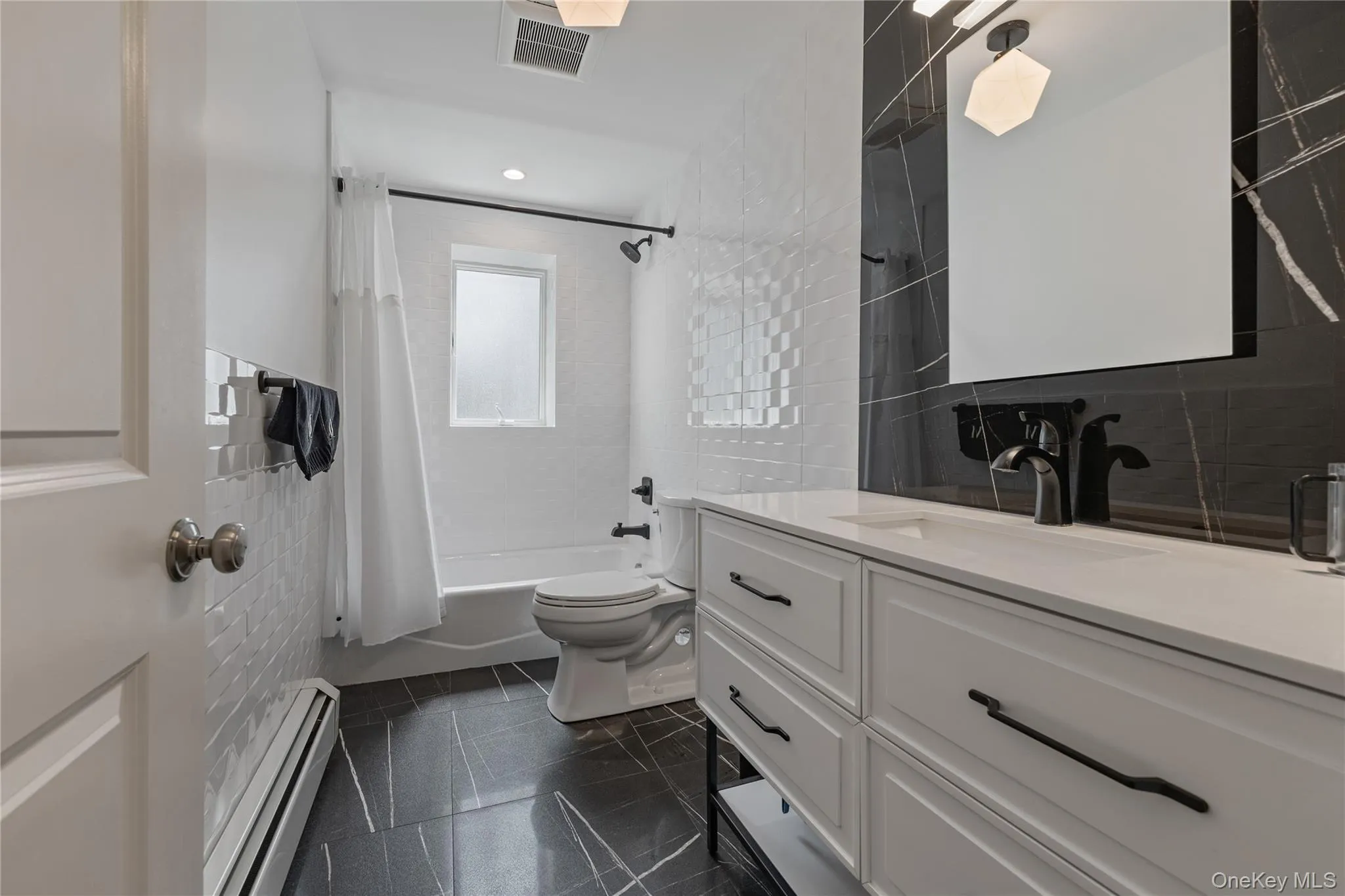 Full bathroom with tile walls, vanity, a baseboard heating unit, shower / tub combo, and dark tile patterned flooring Full bathroom with tile walls, vanity, a baseboard heating unit, shower / tub combo, and dark tile patterned flooring