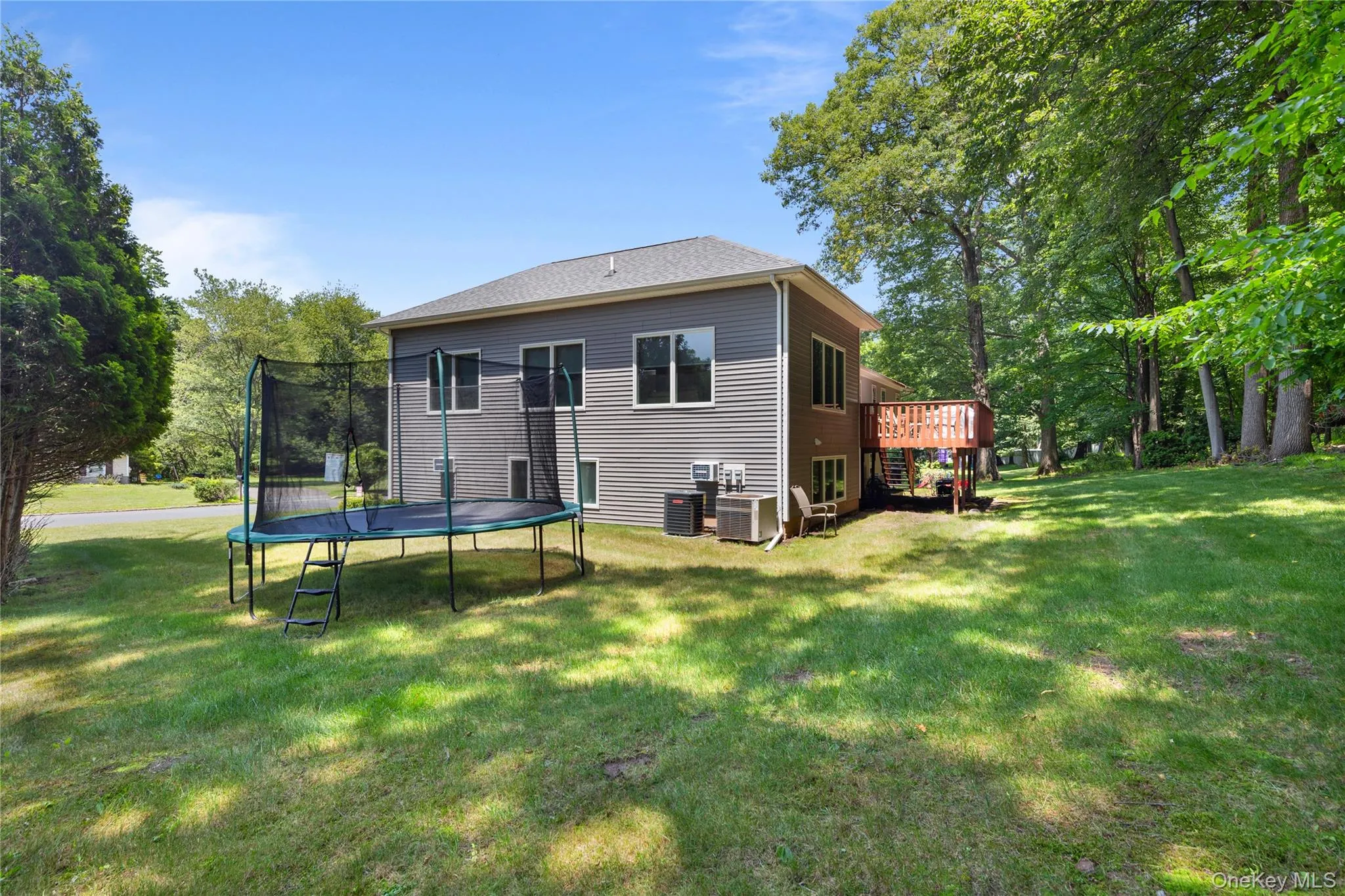 Rear view of house featuring a trampoline, a wooden deck, and a yard Rear view of house featuring a trampoline, a wooden deck, and a yard