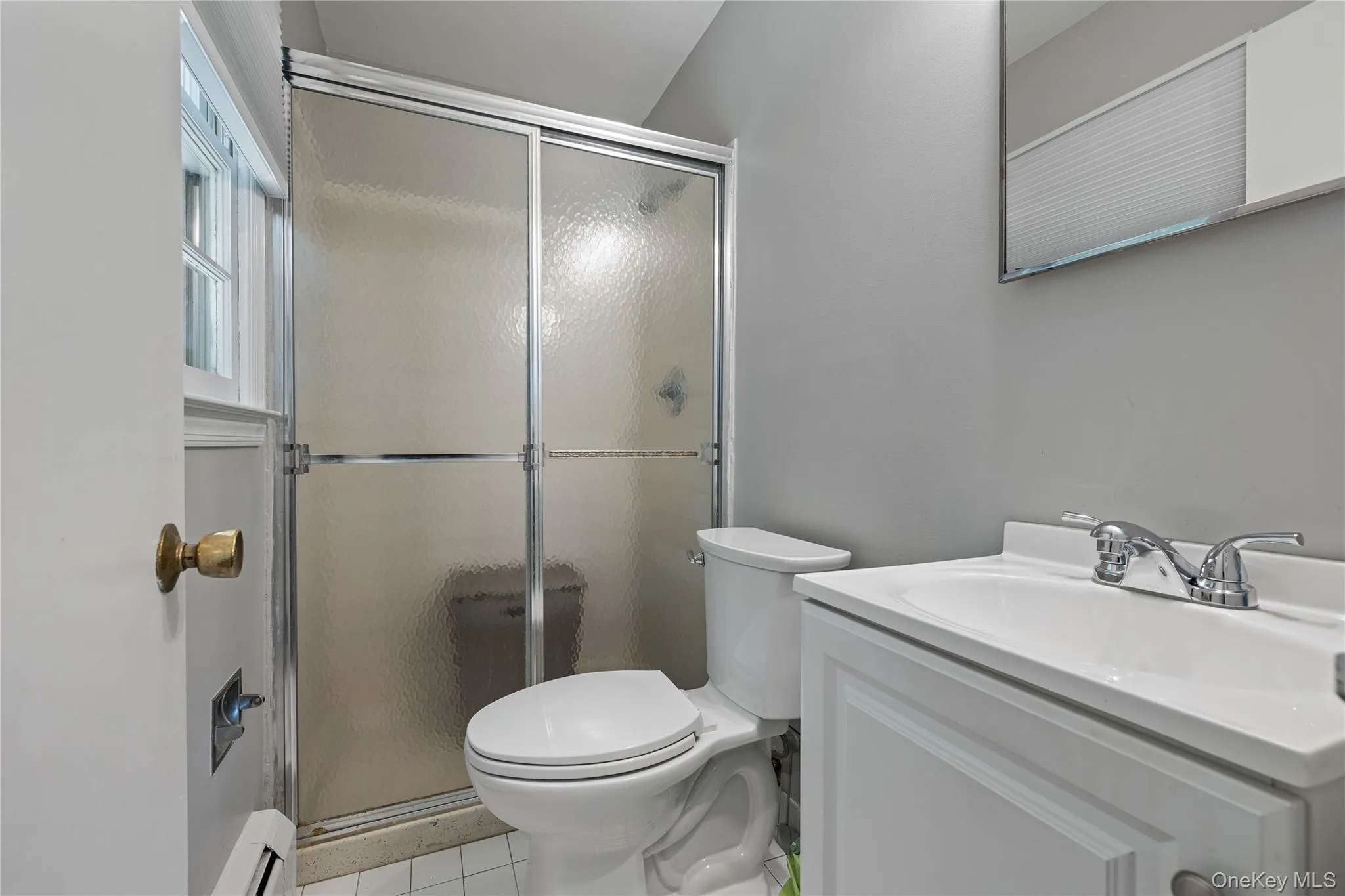Full bath featuring light tile patterned flooring, vanity, a stall shower, and a baseboard radiator Full bath featuring light tile patterned flooring, vanity, a stall shower, and a baseboard radiator