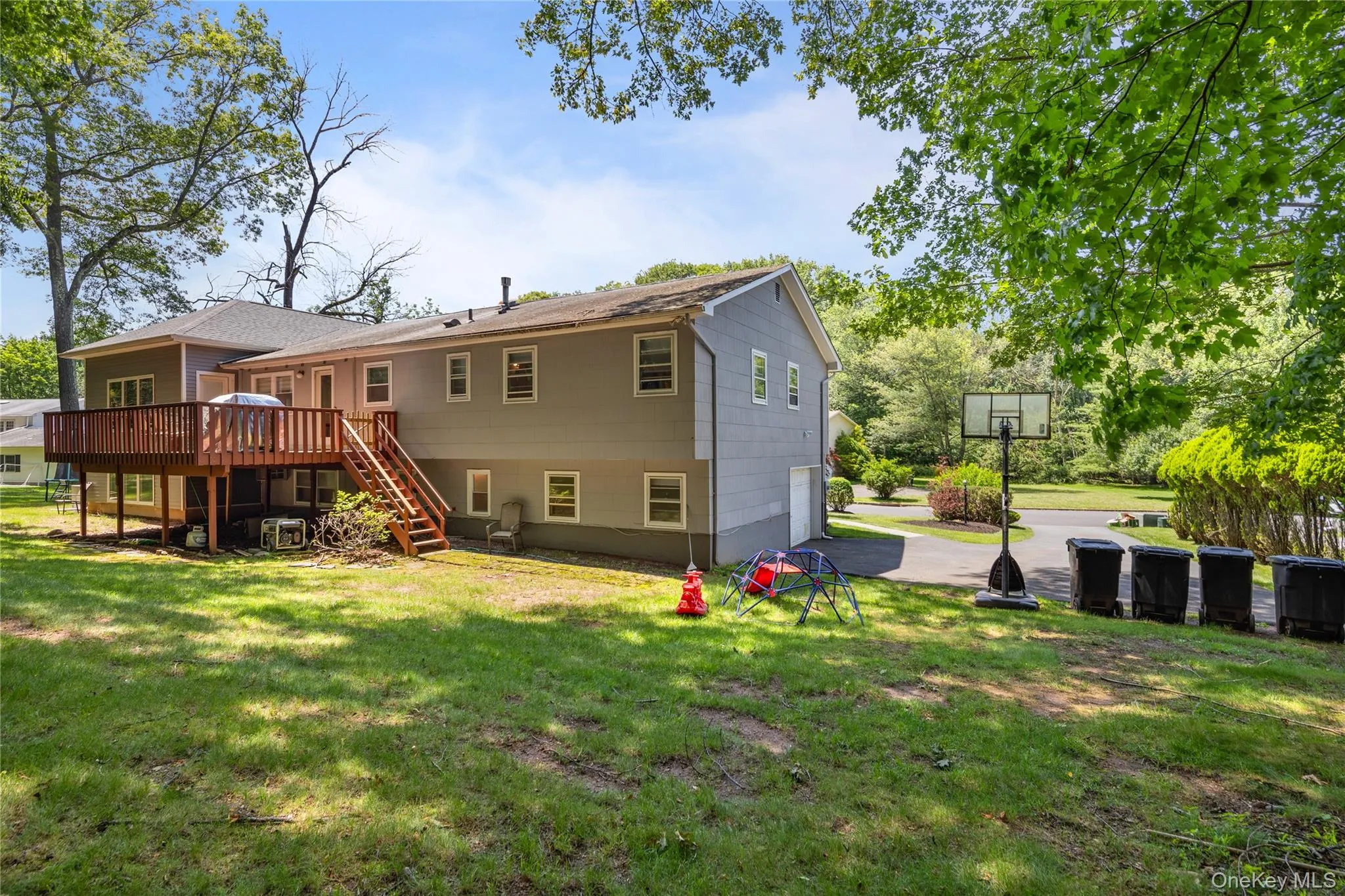 Back of property featuring stairs, a yard, a garage, a deck, and driveway Back of property featuring stairs, a yard, a garage, a deck, and driveway