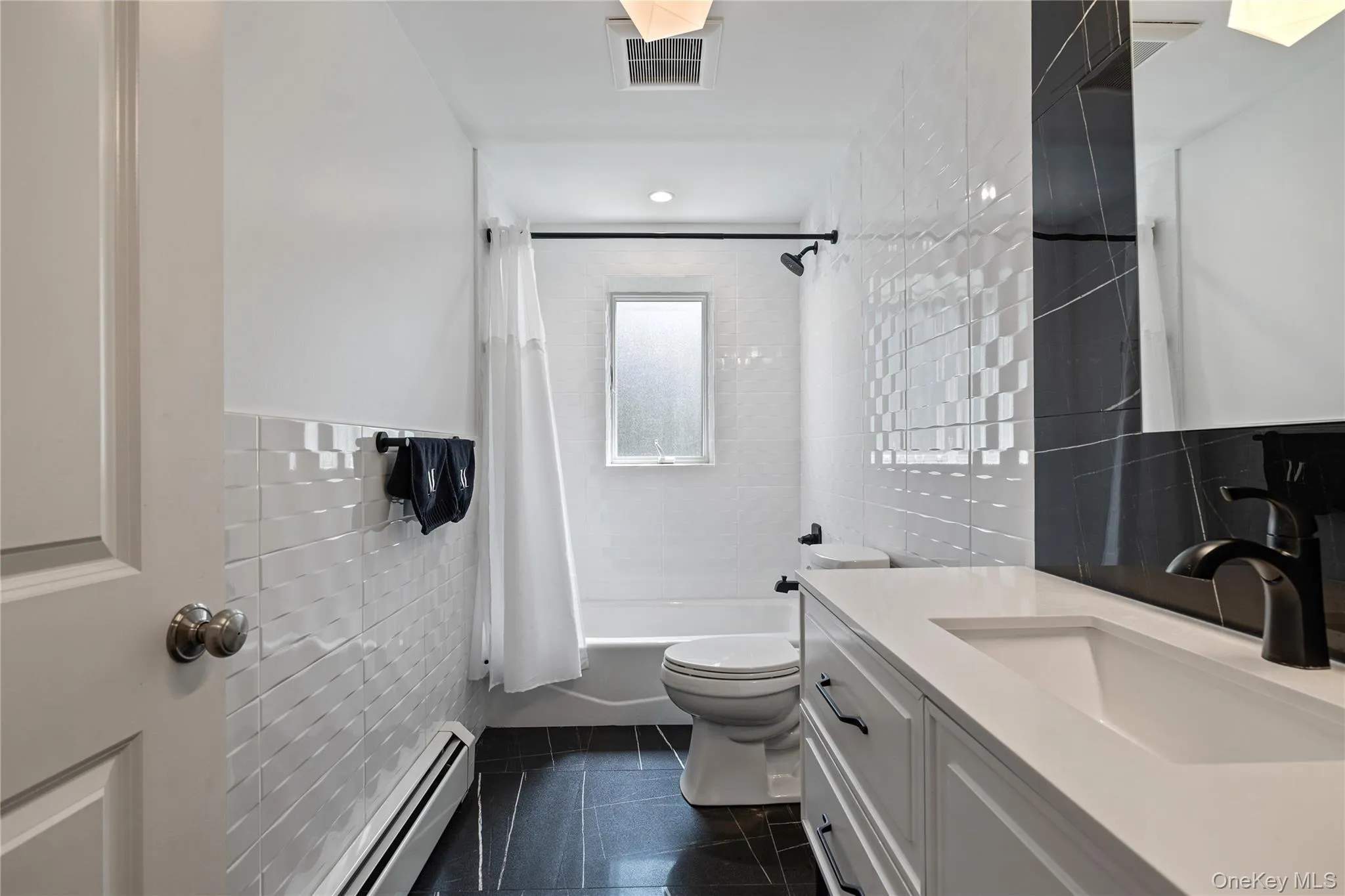 Full bathroom featuring tile walls, shower / bath combo, a baseboard radiator, vanity, and dark tile patterned floors Full bathroom featuring tile walls, shower / bath combo, a baseboard radiator, vanity, and dark tile patterned floors