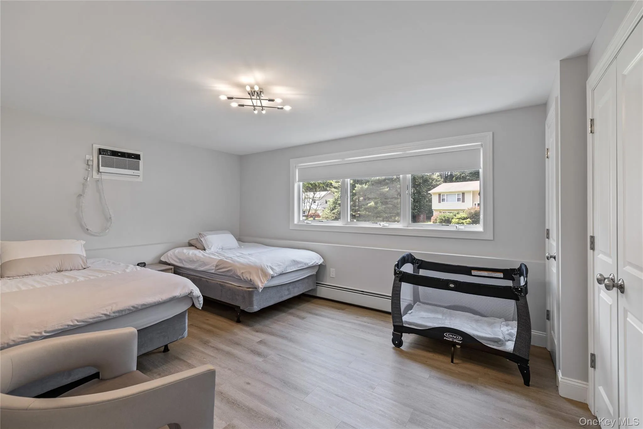 Bedroom featuring light wood-type flooring, an AC wall unit, and a baseboard heating unit Bedroom featuring light wood-type flooring, an AC wall unit, and a baseboard heating unit