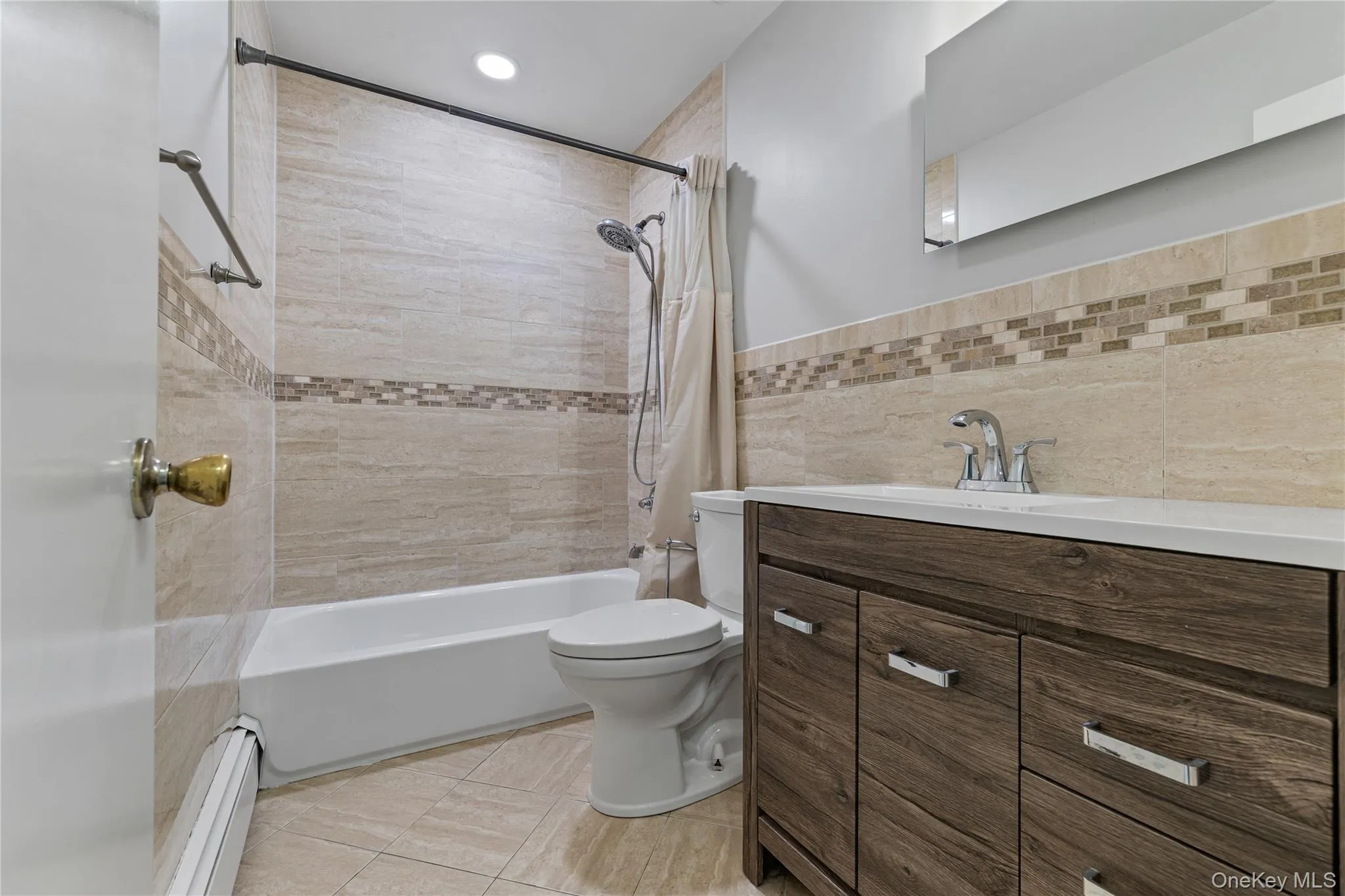 Full bathroom featuring shower / bath combination with curtain, tile walls, vanity, a baseboard radiator, and light tile patterned flooring Full bathroom featuring shower / bath combination with curtain, tile walls, vanity, a baseboard radiator, and light tile patterned flooring