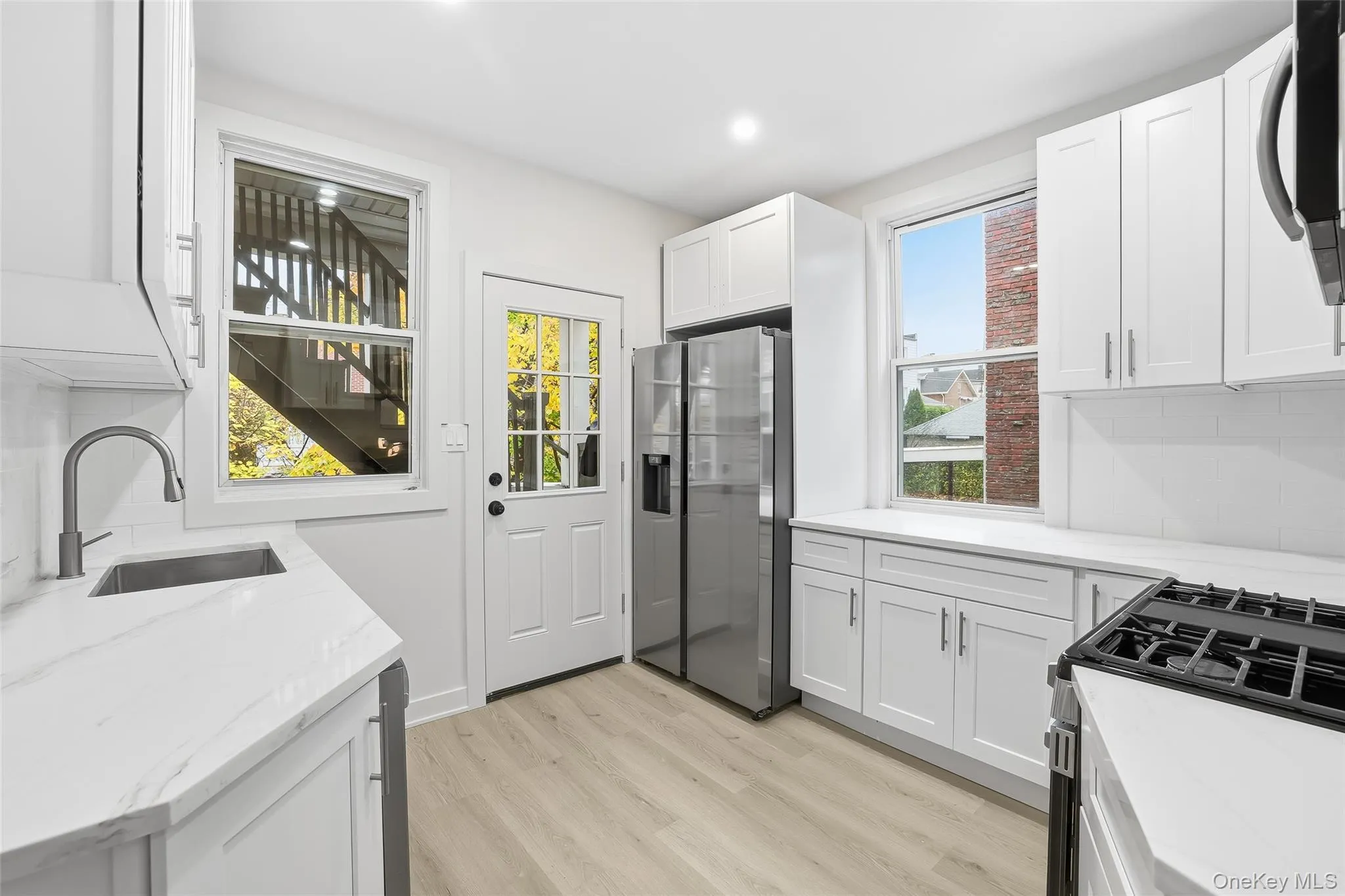 Kitchen with gas range oven, decorative backsplash, stainless steel fridge with ice dispenser, light wood-style floors, and recessed lighting Kitchen with gas range oven, decorative backsplash, stainless steel fridge with ice dispenser, light wood-style floors, and recessed lighting