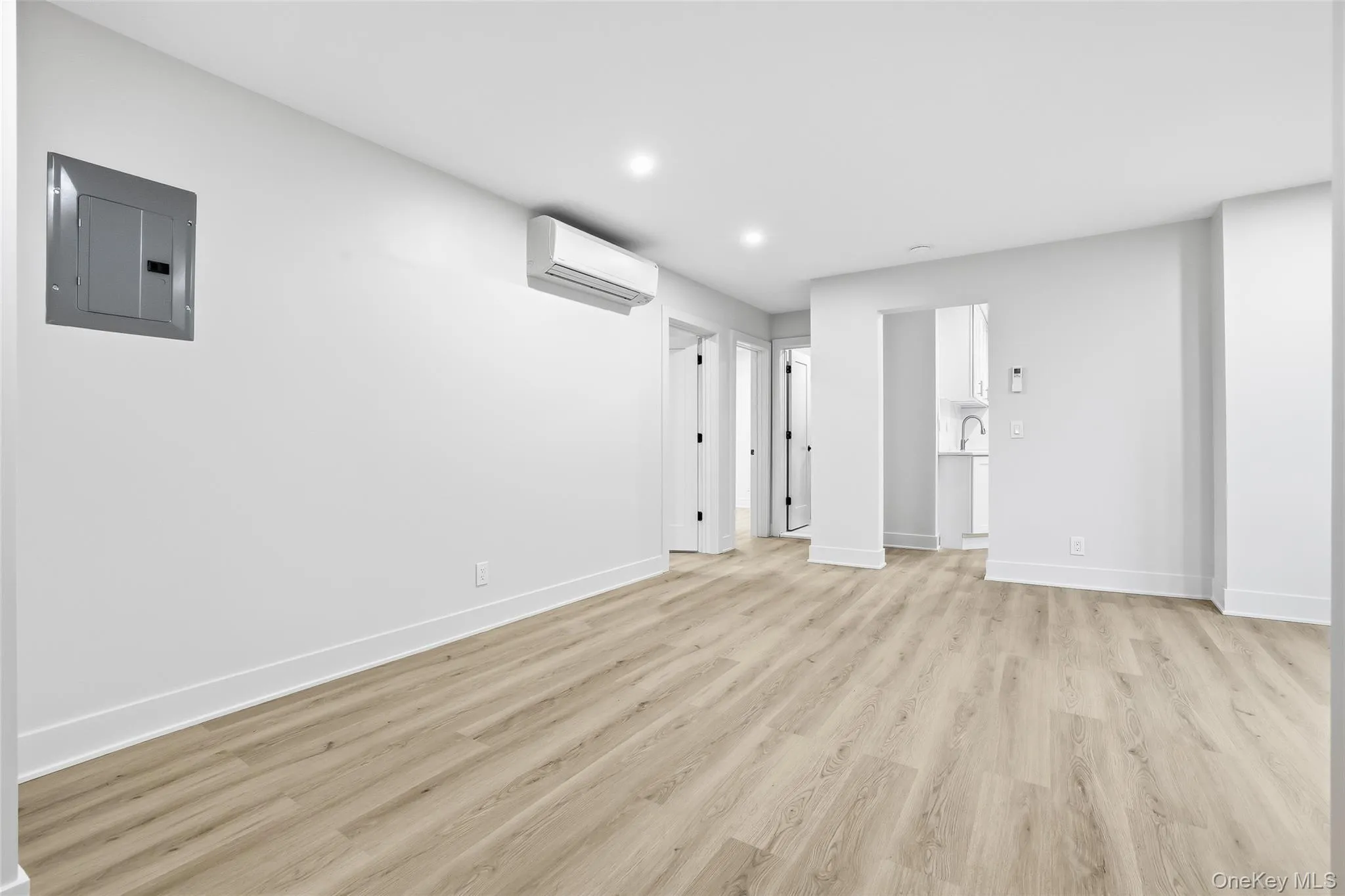 Below grade area featuring electric panel, light wood-style flooring, recessed lighting, and an AC wall unit Below grade area featuring electric panel, light wood-style flooring, recessed lighting, and an AC wall unit