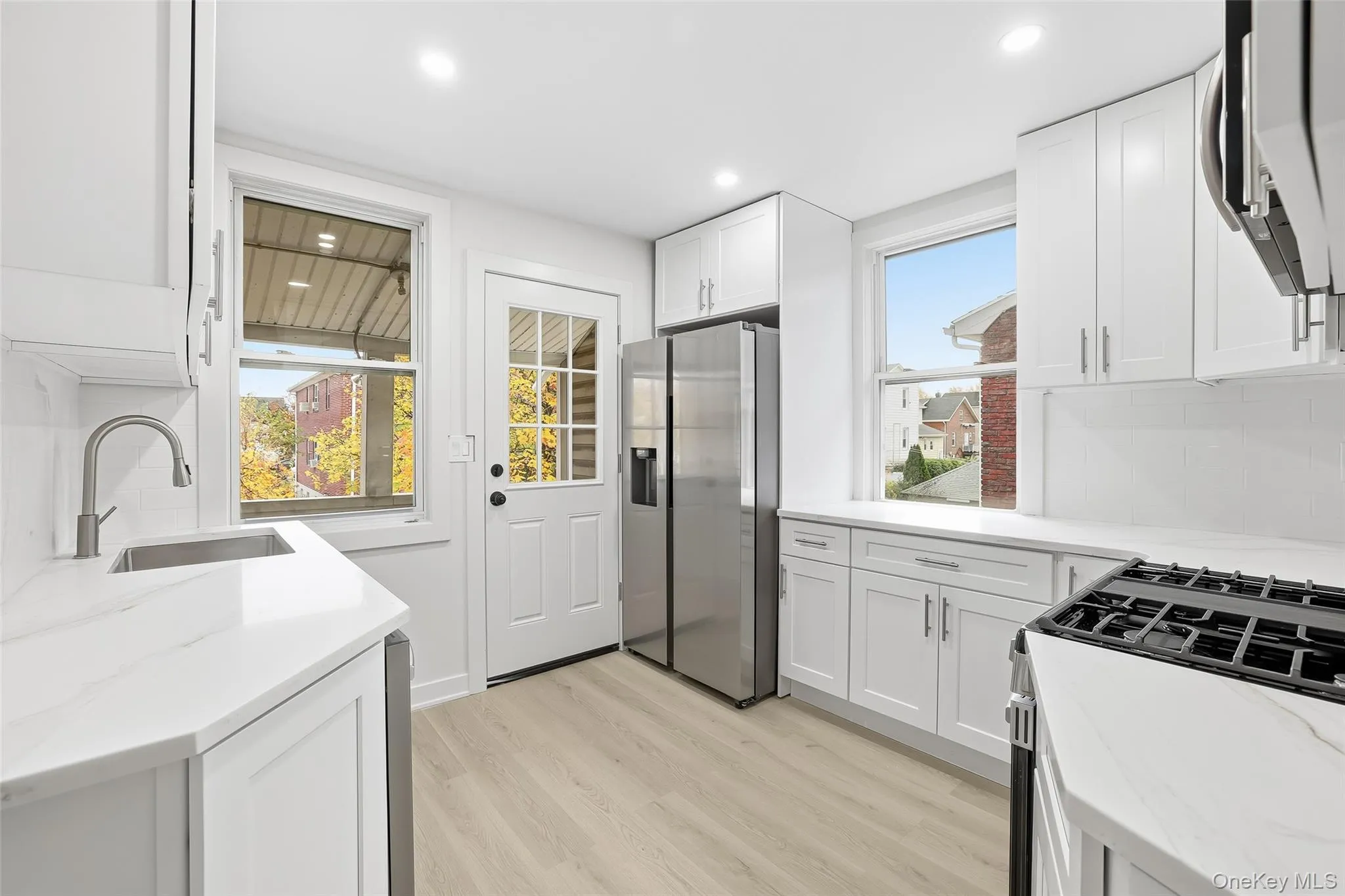 Kitchen with decorative backsplash, appliances with stainless steel finishes, light wood-style floors, light stone counters, and recessed lighting Kitchen with decorative backsplash, appliances with stainless steel finishes, light wood-style floors, light stone counters, and recessed lighting