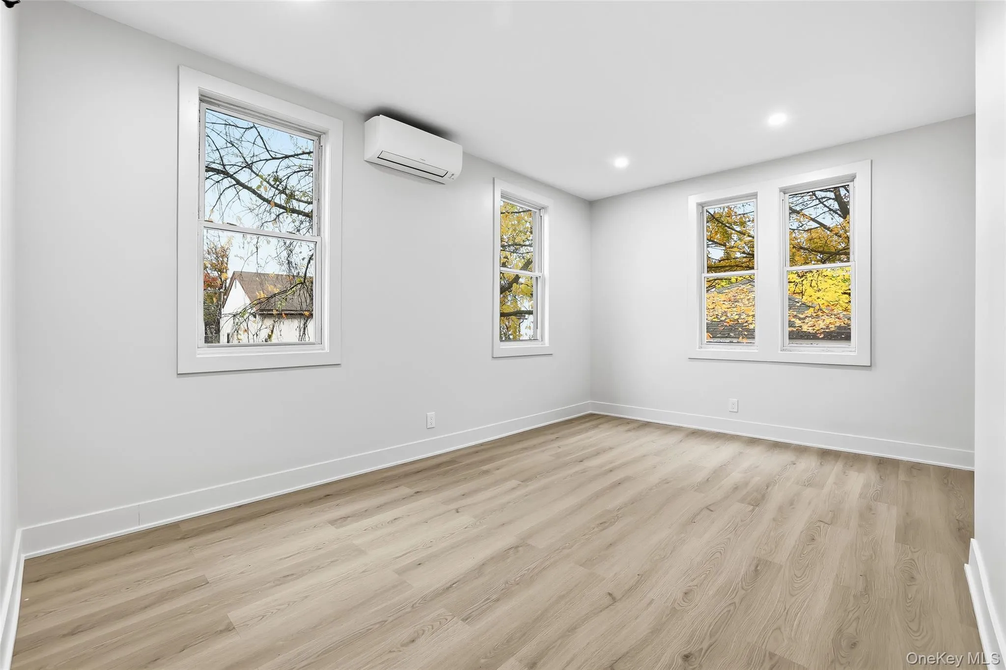Unfurnished room with light wood-style flooring, healthy amount of natural light, recessed lighting, and an AC wall unit Unfurnished room with light wood-style flooring, healthy amount of natural light, recessed lighting, and an AC wall unit