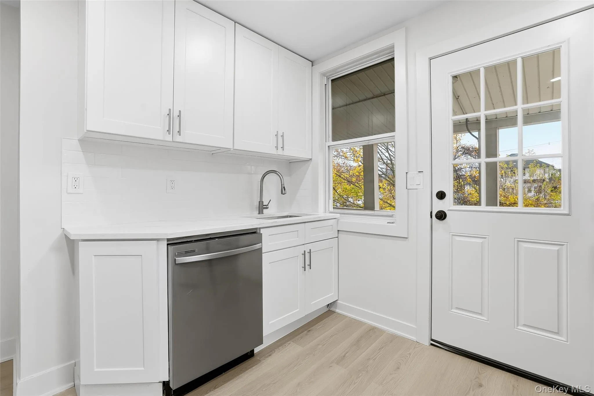Kitchen featuring stainless steel dishwasher, white cabinetry, decorative backsplash, and light wood-style floors Kitchen featuring stainless steel dishwasher, white cabinetry, decorative backsplash, and light wood-style floors