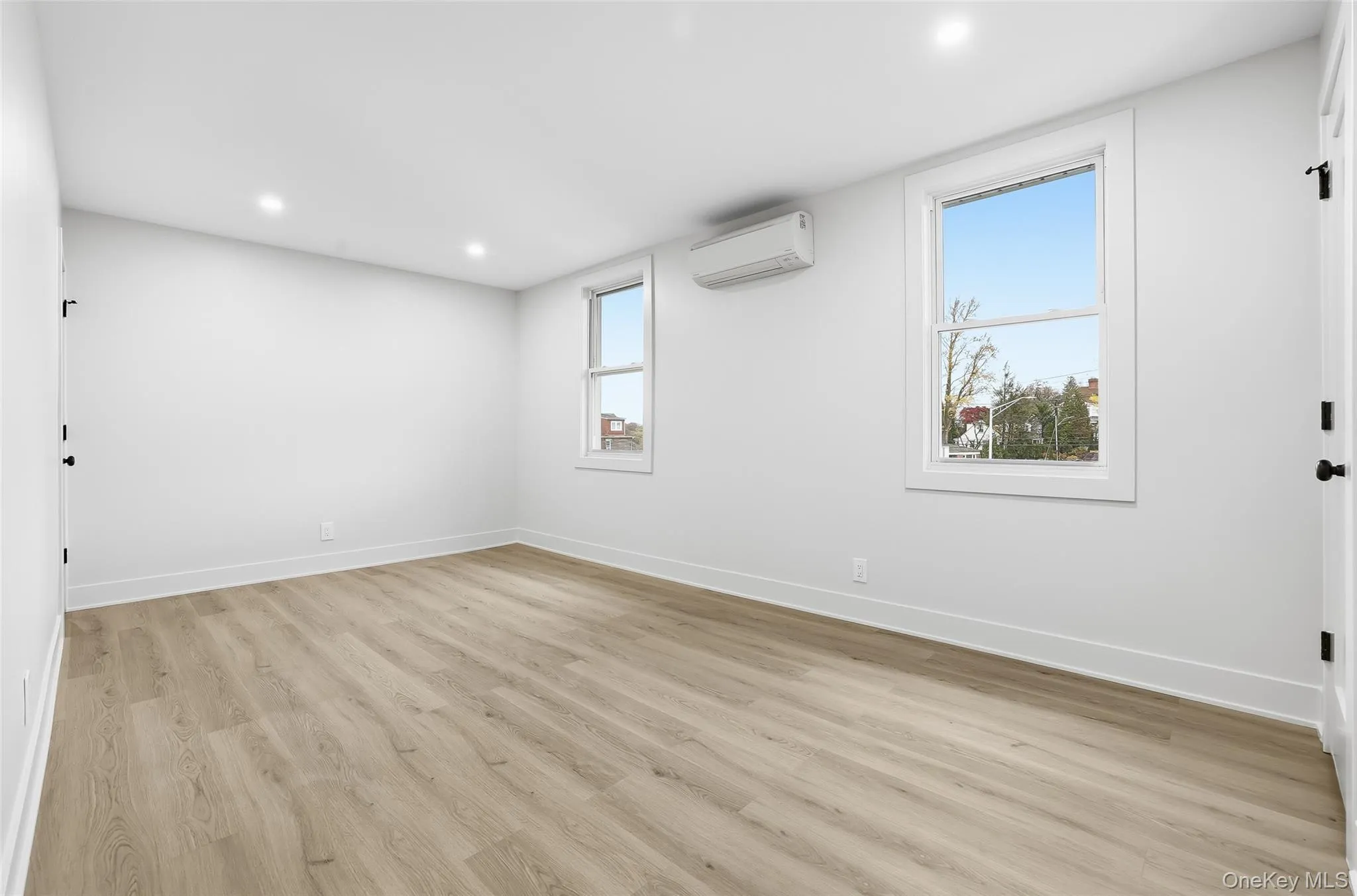 Empty room featuring light wood-style flooring, recessed lighting, and a wall mounted air conditioner Empty room featuring light wood-style flooring, recessed lighting, and a wall mounted air conditioner