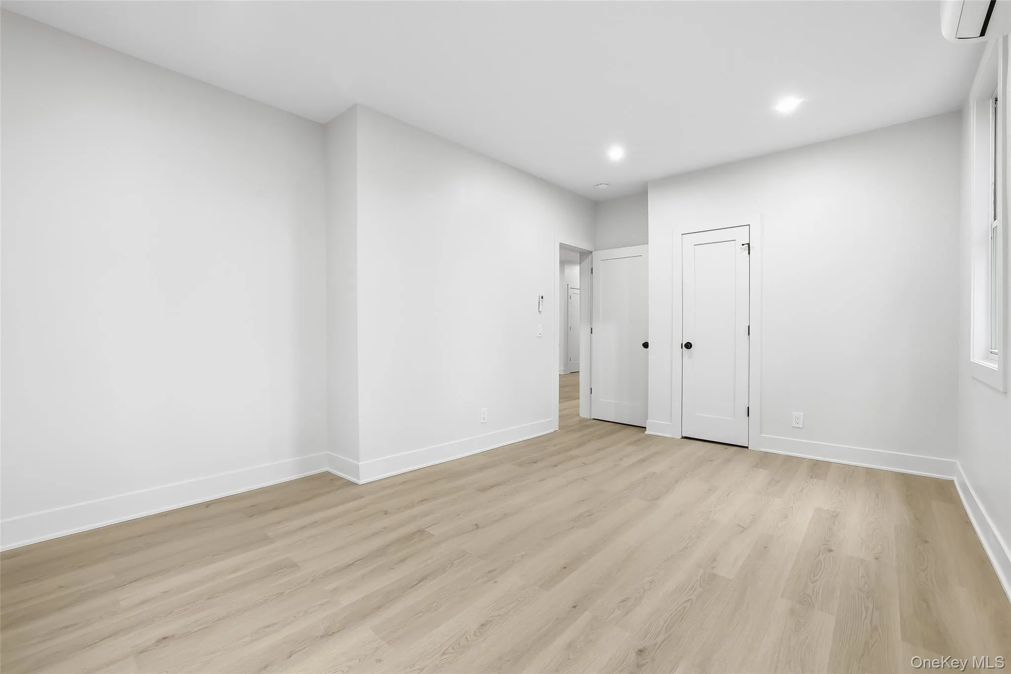 Unfurnished bedroom with light wood-style floors, an AC wall unit, and recessed lighting Unfurnished bedroom with light wood-style floors, an AC wall unit, and recessed lighting