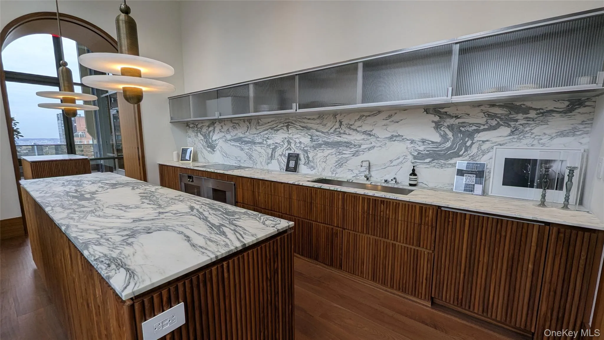Kitchen featuring a kitchen island, light stone countertops, decorative light fixtures, and brown cabinetry Kitchen featuring a kitchen island, light stone countertops, decorative light fixtures, and brown cabinetry