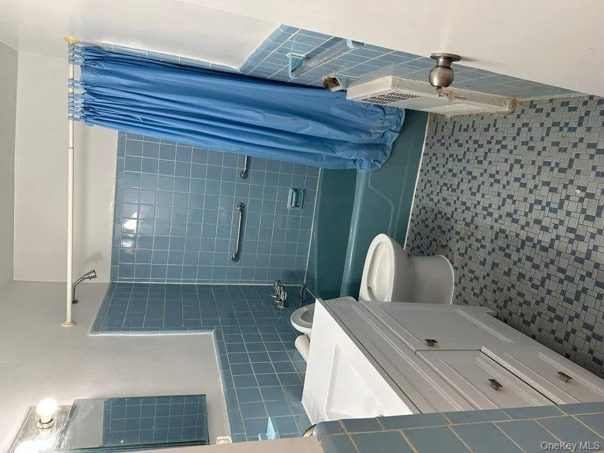 Bathroom with tile walls, shower / bath combination with curtain, vanity, radiator heating unit, and wainscoting Bathroom with tile walls, shower / bath combination with curtain, vanity, radiator heating unit, and wainscoting