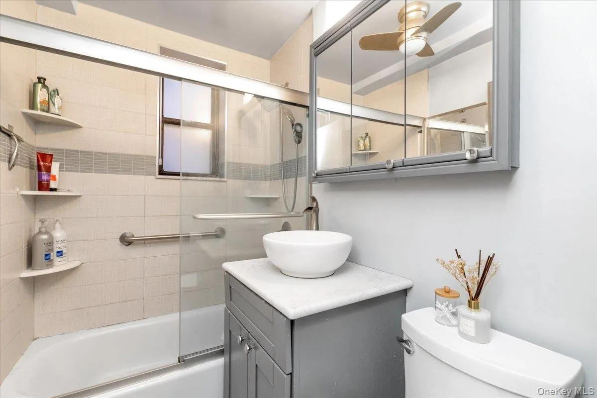 Bathroom featuring vanity, shower / bath combination with glass door, and a ceiling fan Bathroom featuring vanity, shower / bath combination with glass door, and a ceiling fan