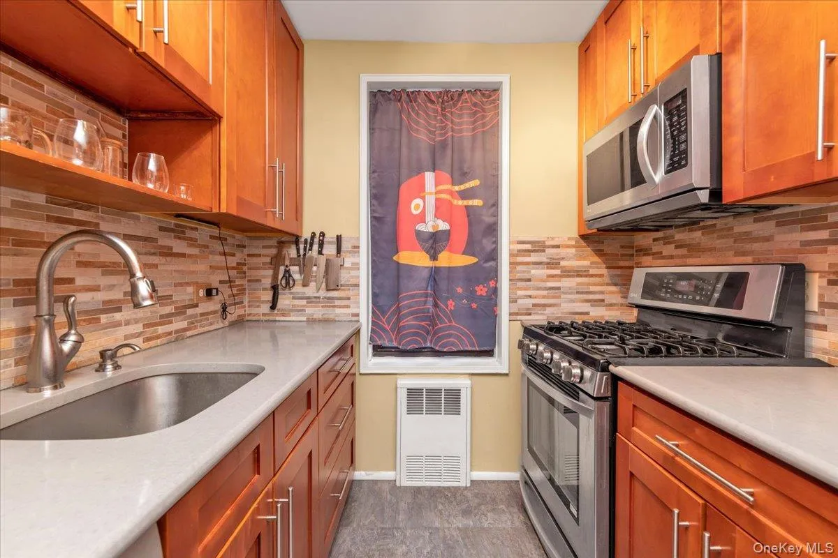 Kitchen featuring appliances with stainless steel finishes, brown cabinetry, tasteful backsplash, and light stone counters Kitchen featuring appliances with stainless steel finishes, brown cabinetry, tasteful backsplash, and light stone counters