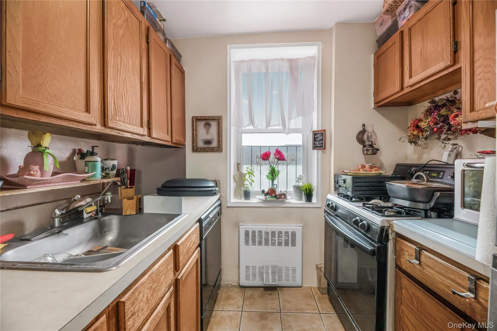 Kitchen with black appliances, radiator, brown cabinetry, light tile patterned floors, and light countertops Kitchen with black appliances, radiator, brown cabinetry, light tile patterned floors, and light countertops