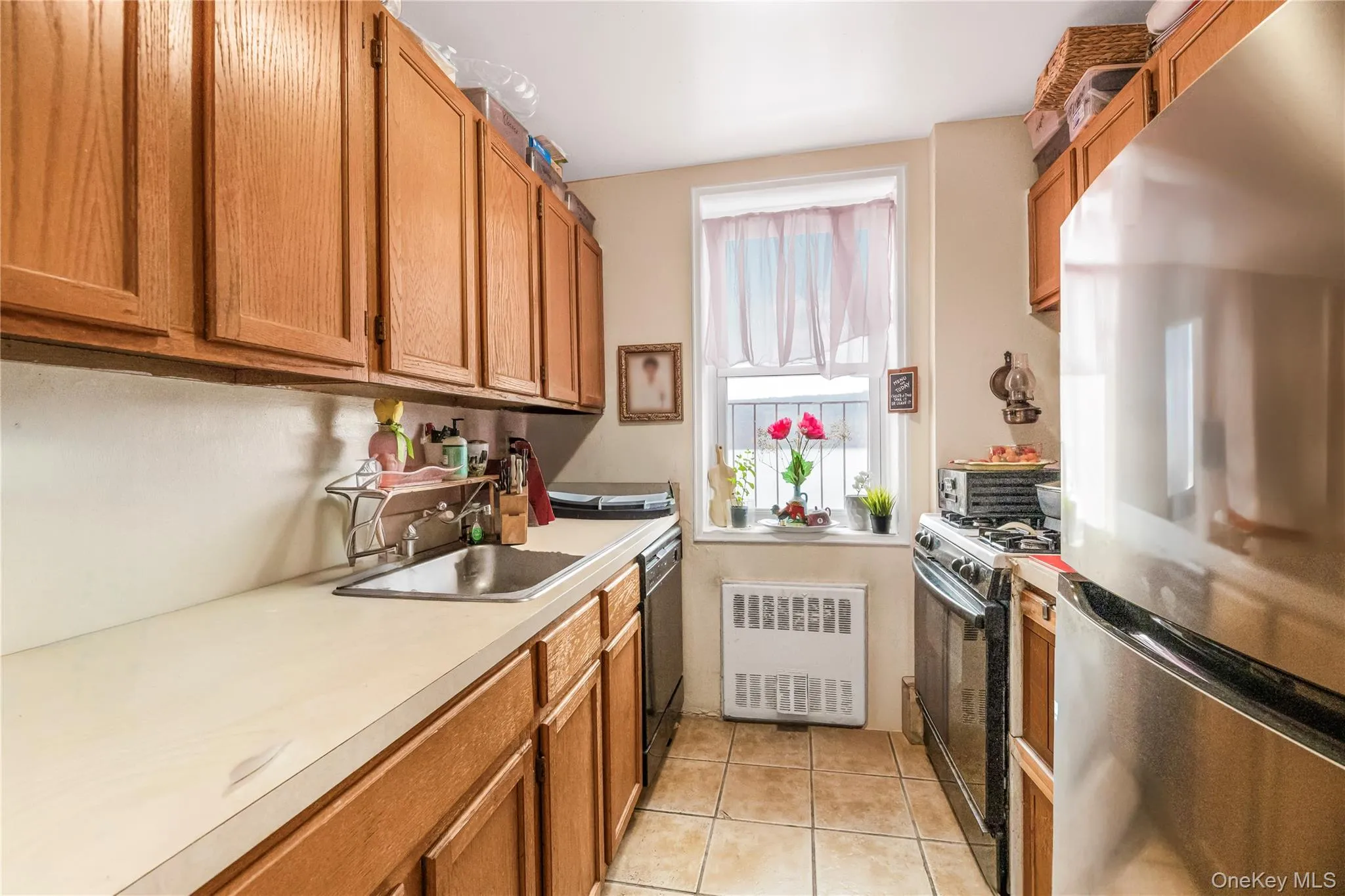 Kitchen featuring black appliances, brown cabinets, radiator, light countertops, and light tile patterned floors Kitchen featuring black appliances, brown cabinets, radiator, light countertops, and light tile patterned floors