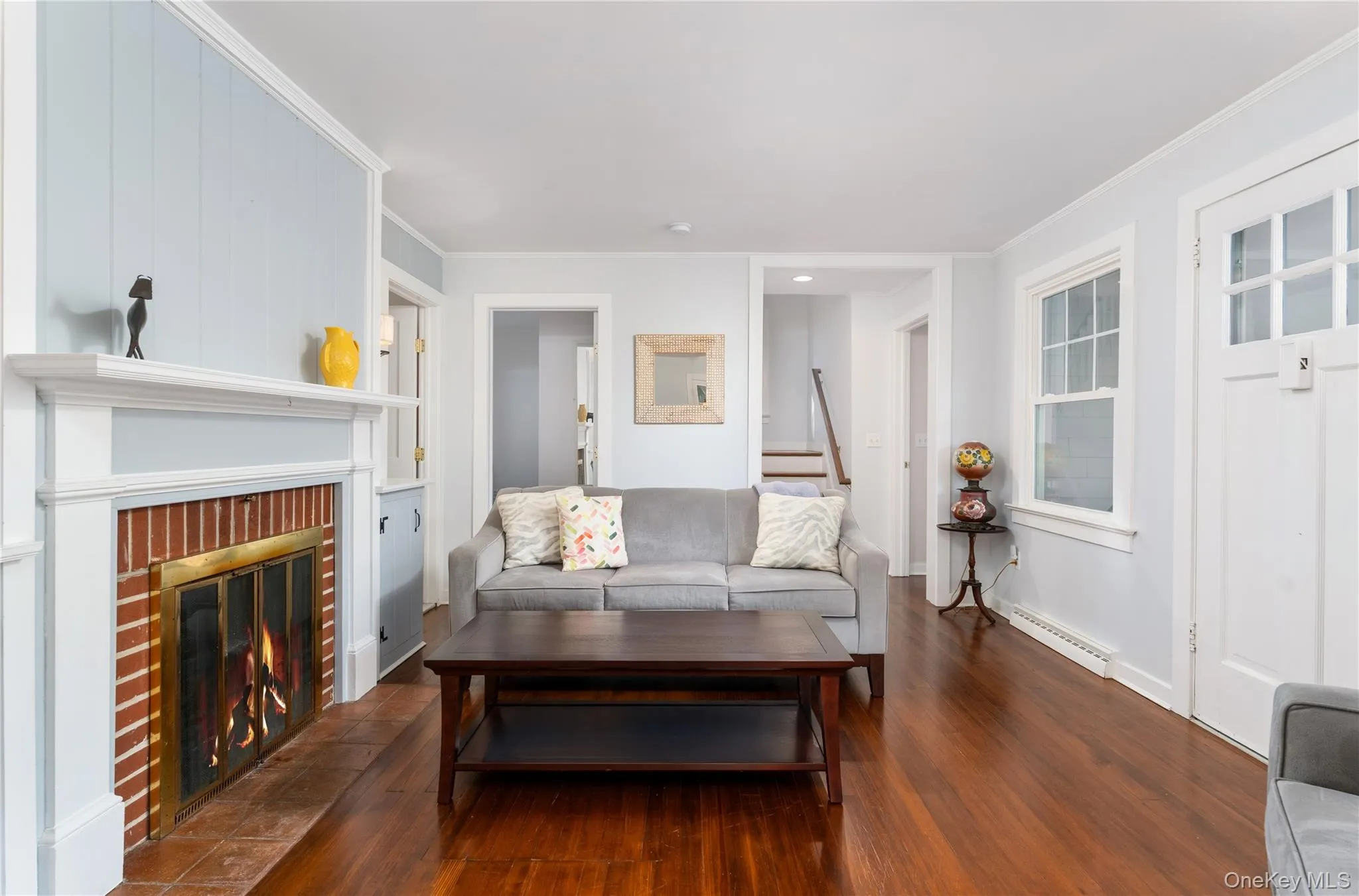 Living room with dark wood-type flooring, crown molding, a fireplace, and baseboard heating Living room with dark wood-type flooring, crown molding, a fireplace, and baseboard heating