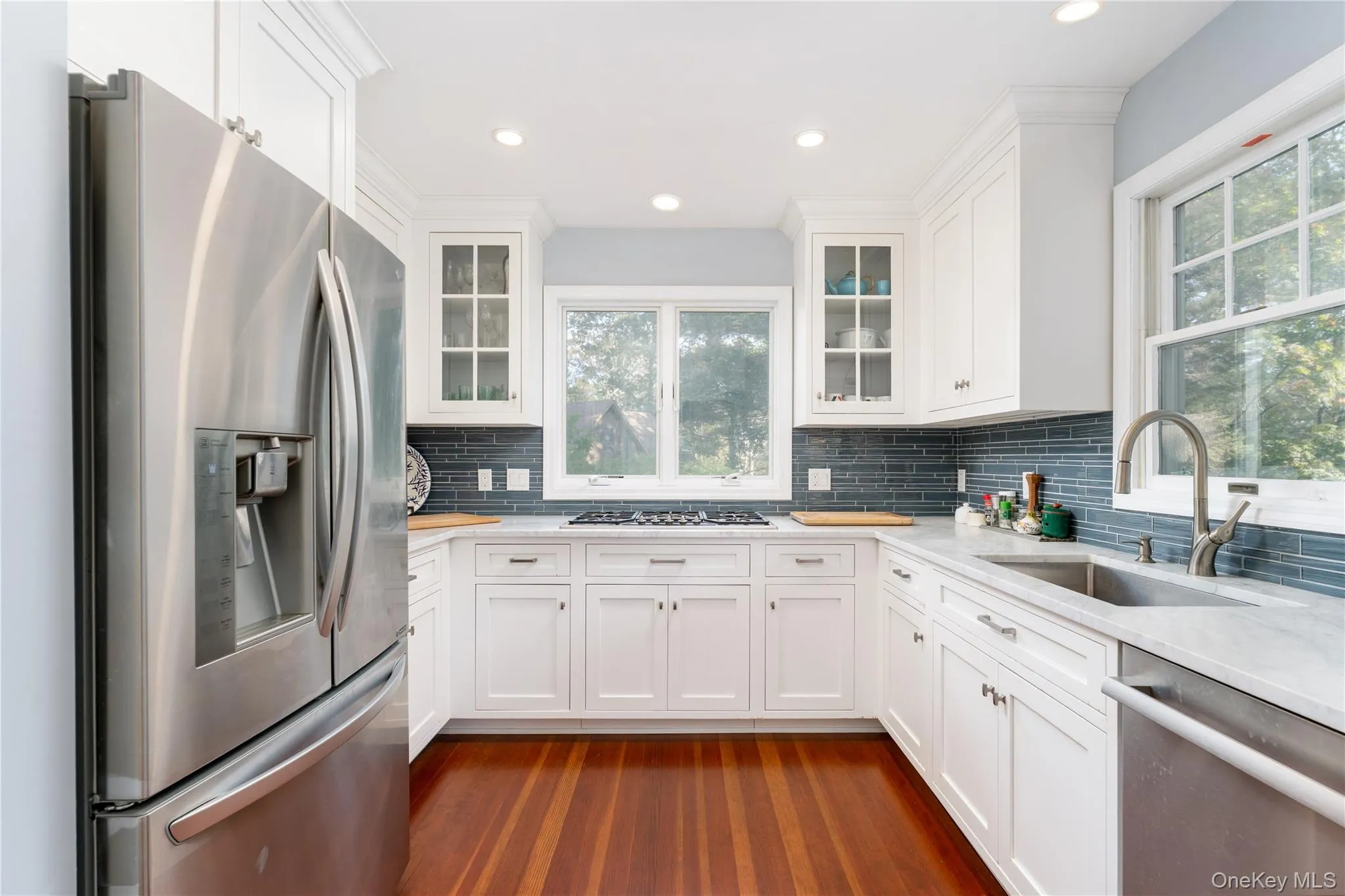 Kitchen with stainless steel appliances, white cabinetry, dark wood-style flooring, backsplash, and recessed lighting Kitchen with stainless steel appliances, white cabinetry, dark wood-style flooring, backsplash, and recessed lighting