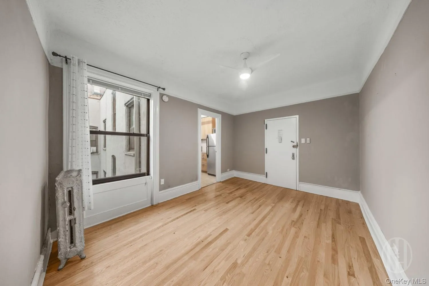 Unfurnished living room from opposite perspective with light wood-style floors, radiator, ceiling fan, ensuite bathroom, and a textured ceiling Unfurnished living room from opposite perspective with light wood-style floors, radiator, ceiling fan, ensuite bathroom, and a textured ceiling