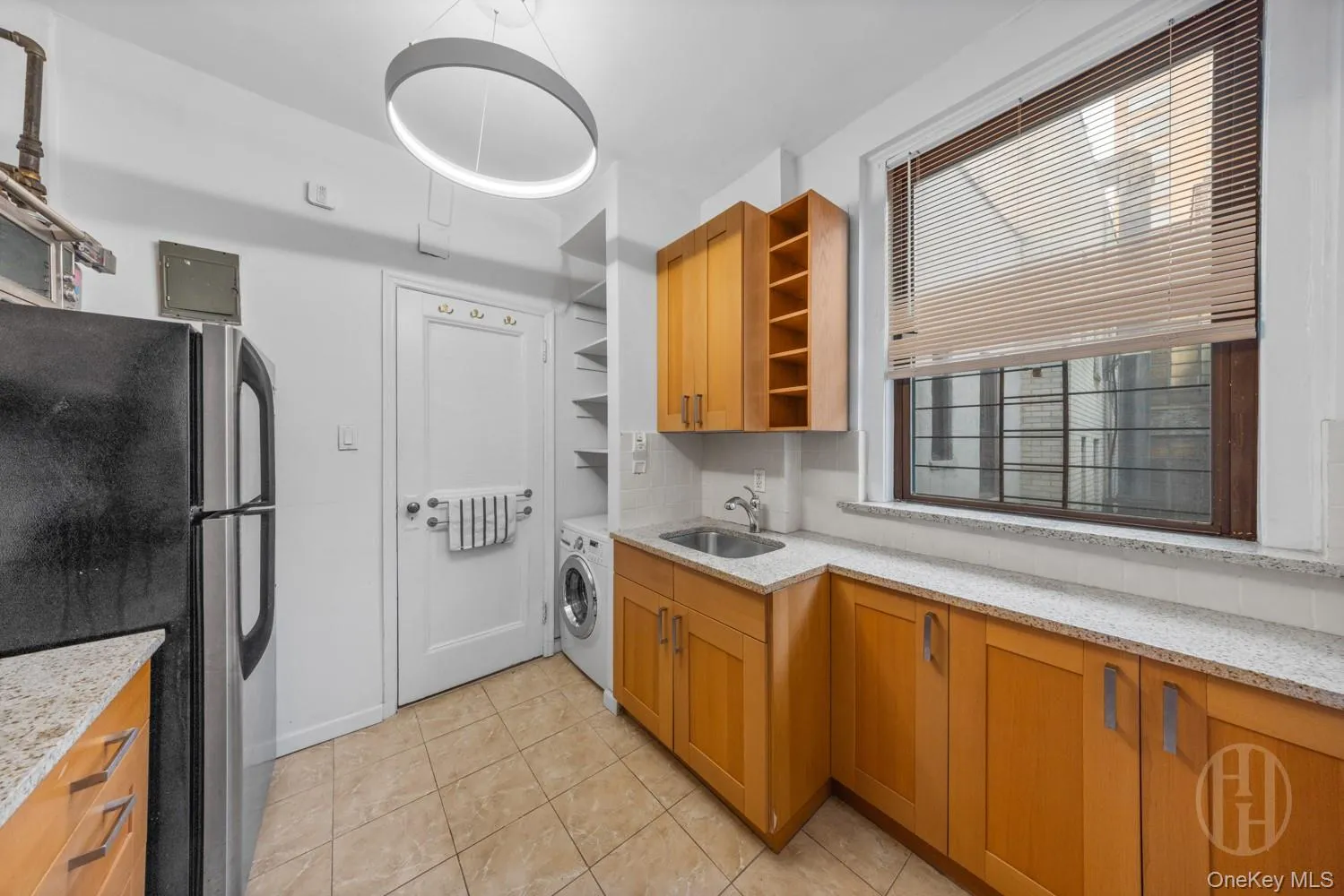 Kitchen featuring freestanding refrigerator, open shelves, light stone countertops, light tile patterned flooring, and brown cabinetry Kitchen featuring freestanding refrigerator, open shelves, light stone countertops, light tile patterned flooring, and brown cabinetry