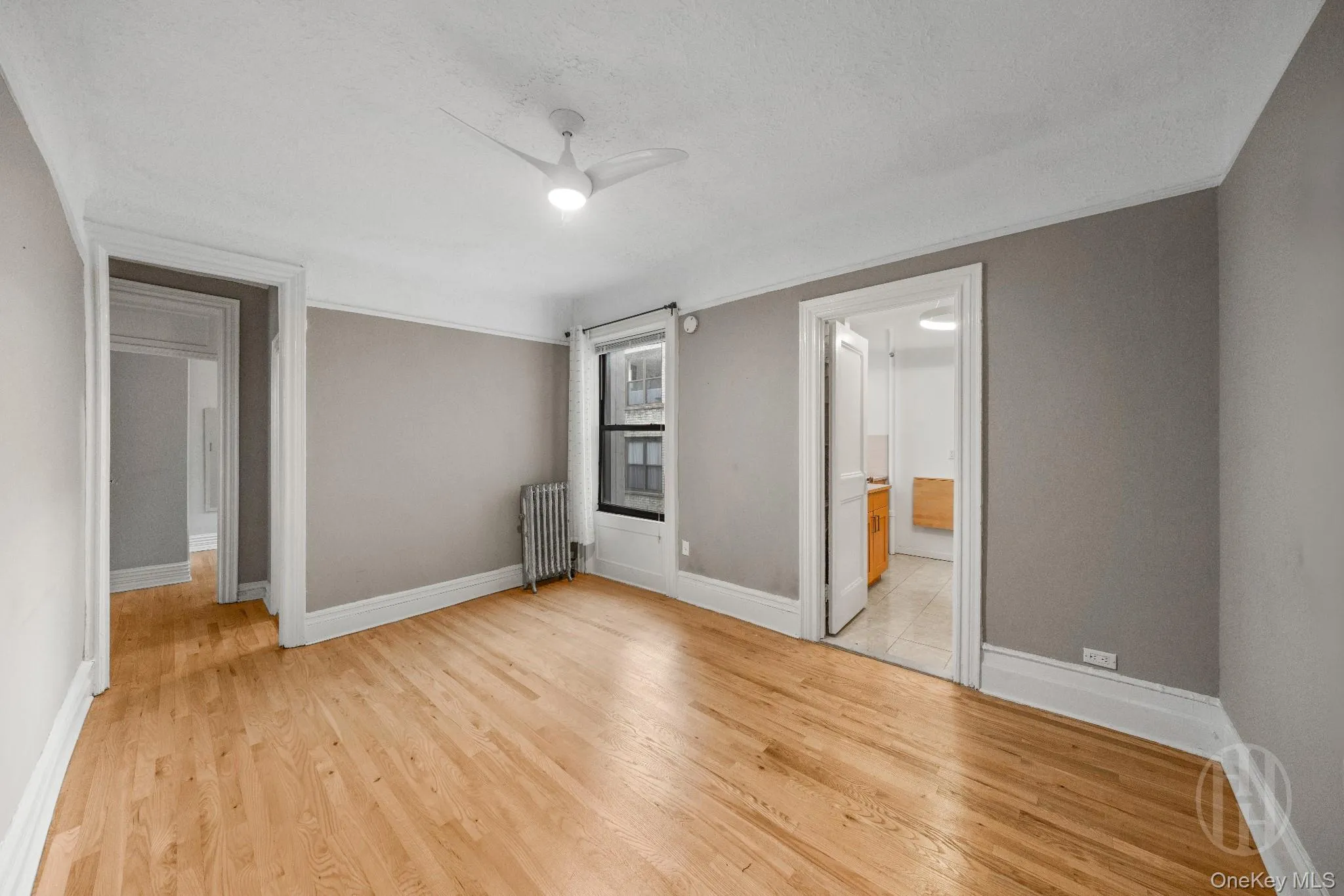 Unfurnished living room with light wood-style floors, radiator, ceiling fan, ensuite bathroom, and a textured ceiling Unfurnished living room with light wood-style floors, radiator, ceiling fan, ensuite bathroom, and a textured ceiling
