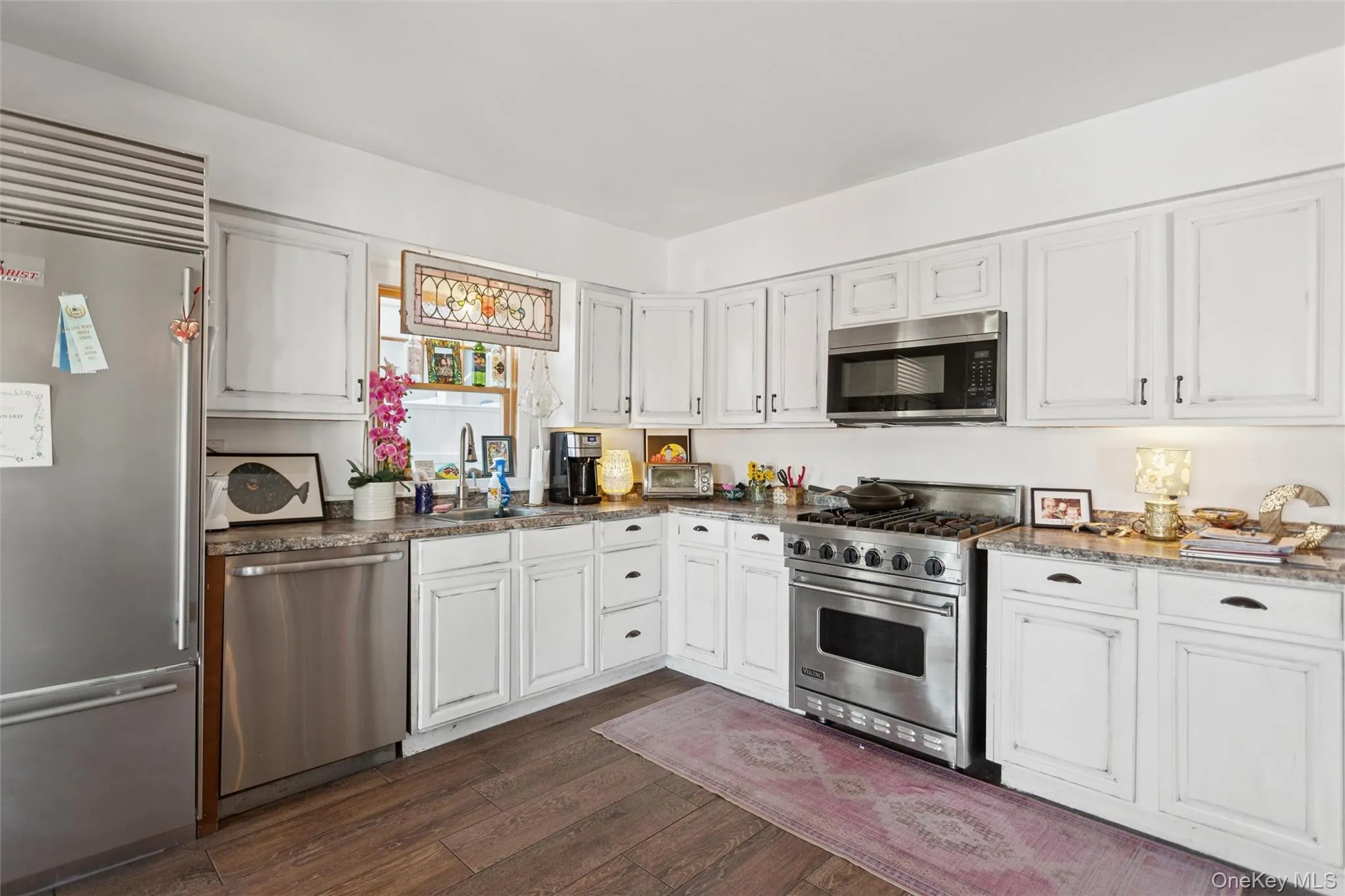 Kitchen with high quality appliances, white cabinets, dark wood finished floors, and dark stone counters Kitchen with high quality appliances, white cabinets, dark wood finished floors, and dark stone counters