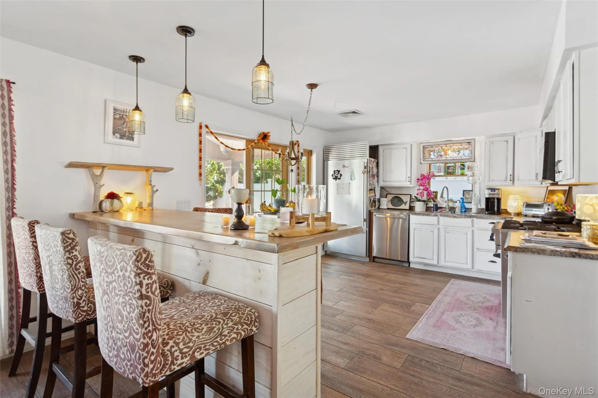 Kitchen with white cabinetry, pendant lighting, a breakfast bar area, dark wood-type flooring, and stainless steel appliances Kitchen with white cabinetry, pendant lighting, a breakfast bar area, dark wood-type flooring, and stainless steel appliances