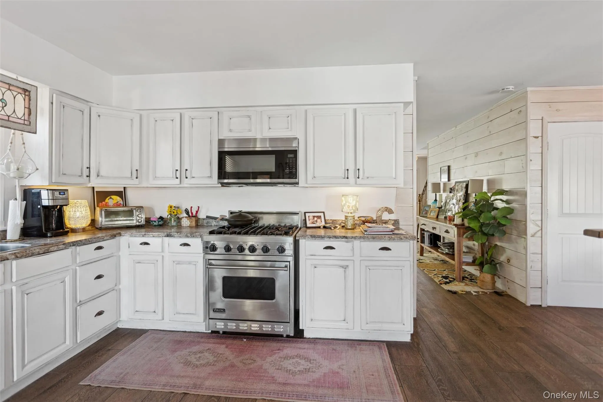 Kitchen with white cabinets, stainless steel appliances, dark wood finished floors, and wooden walls Kitchen with white cabinets, stainless steel appliances, dark wood finished floors, and wooden walls