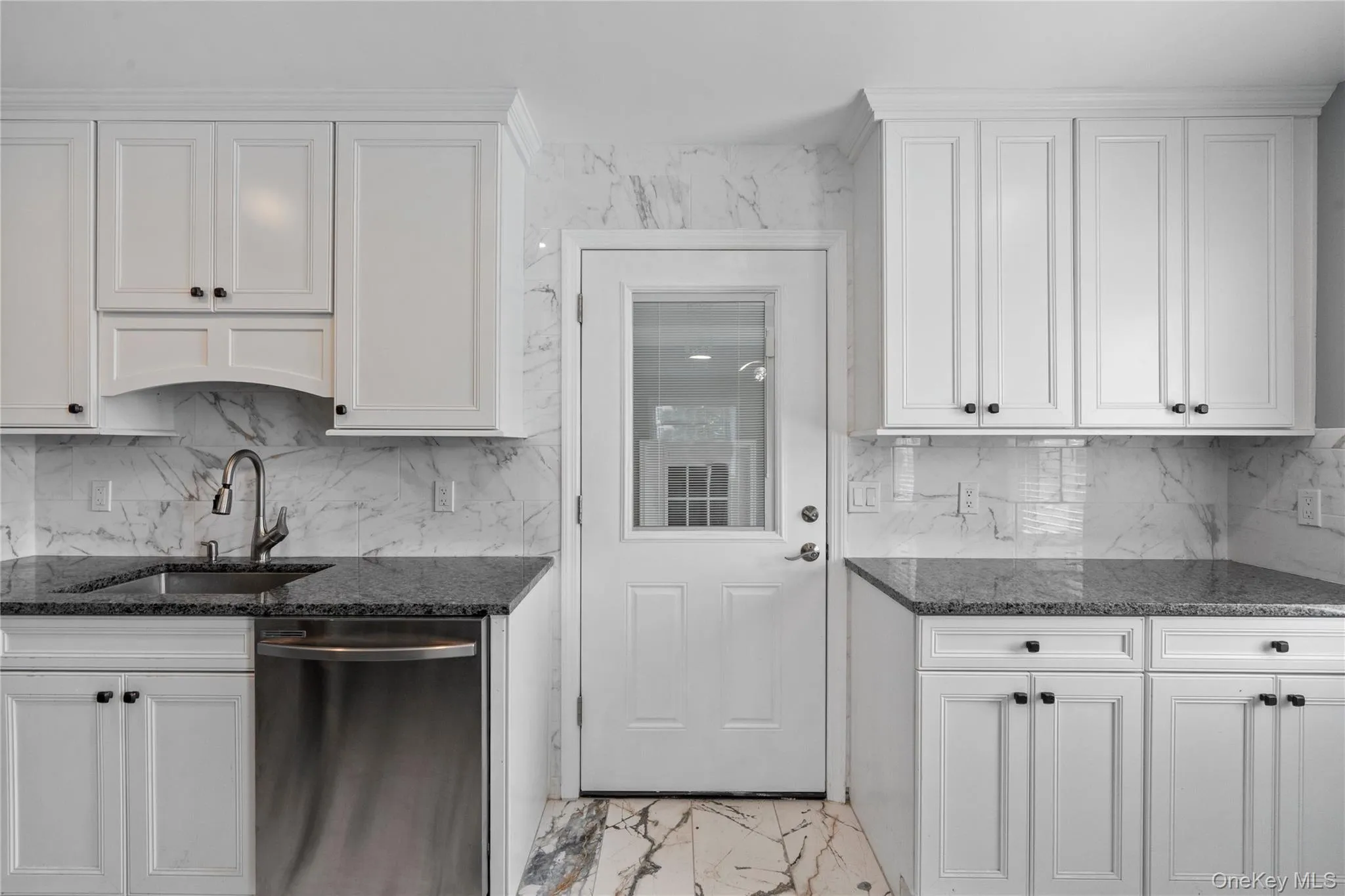 Kitchen featuring white cabinetry, stainless steel dishwasher, dark stone counters, and backsplash Kitchen featuring white cabinetry, stainless steel dishwasher, dark stone counters, and backsplash