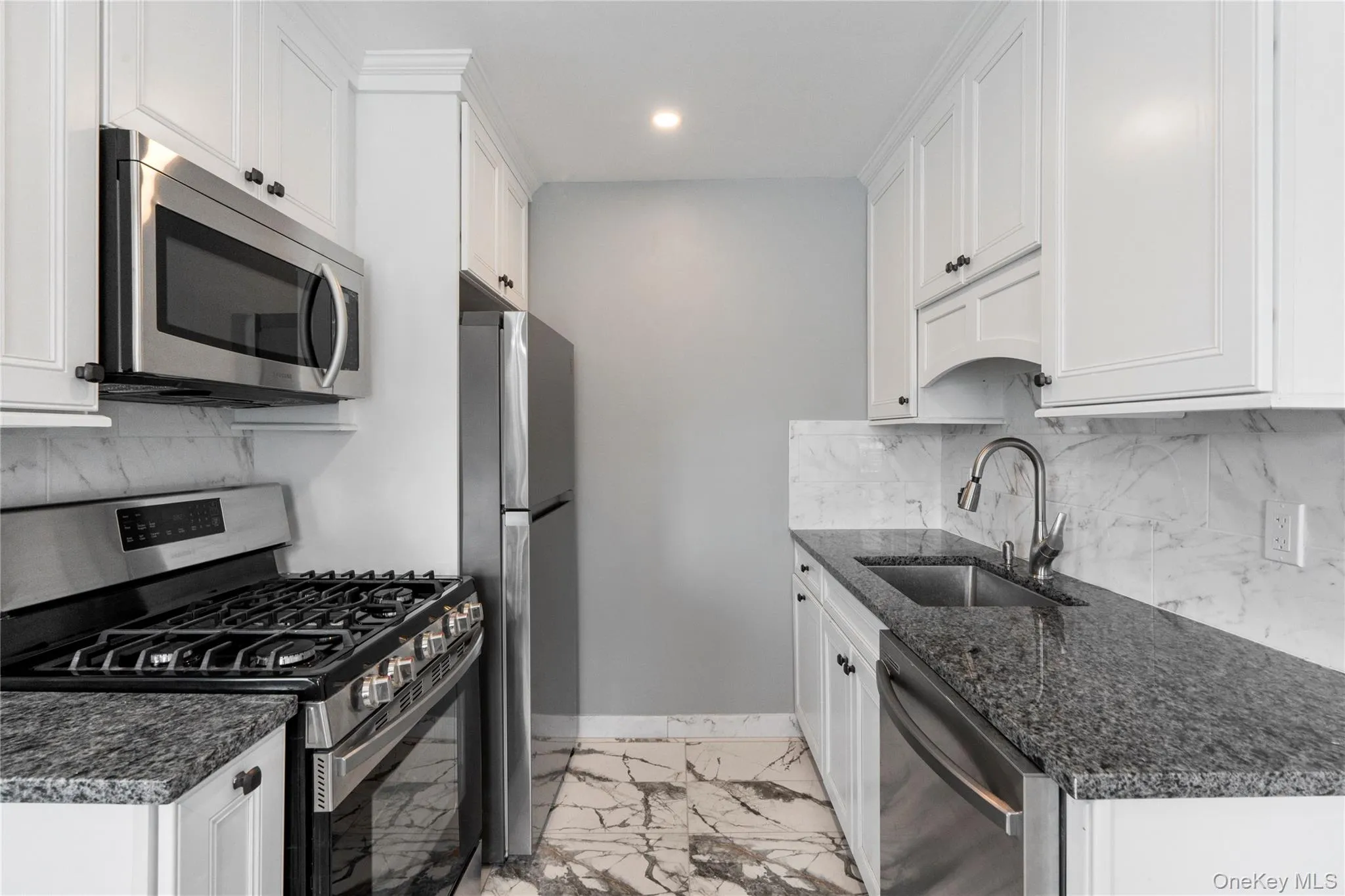 Kitchen with stainless steel appliances, backsplash, light marble finish floors, white cabinetry, and recessed lighting Kitchen with stainless steel appliances, backsplash, light marble finish floors, white cabinetry, and recessed lighting