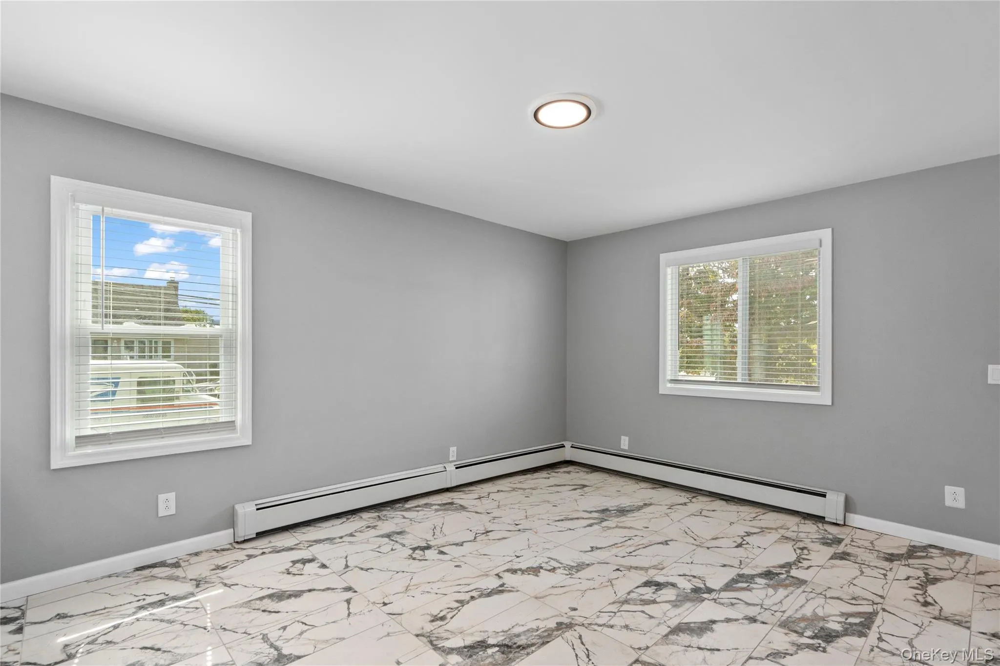 Unfurnished room featuring a baseboard radiator and light marble finish flooring Unfurnished room featuring a baseboard radiator and light marble finish flooring