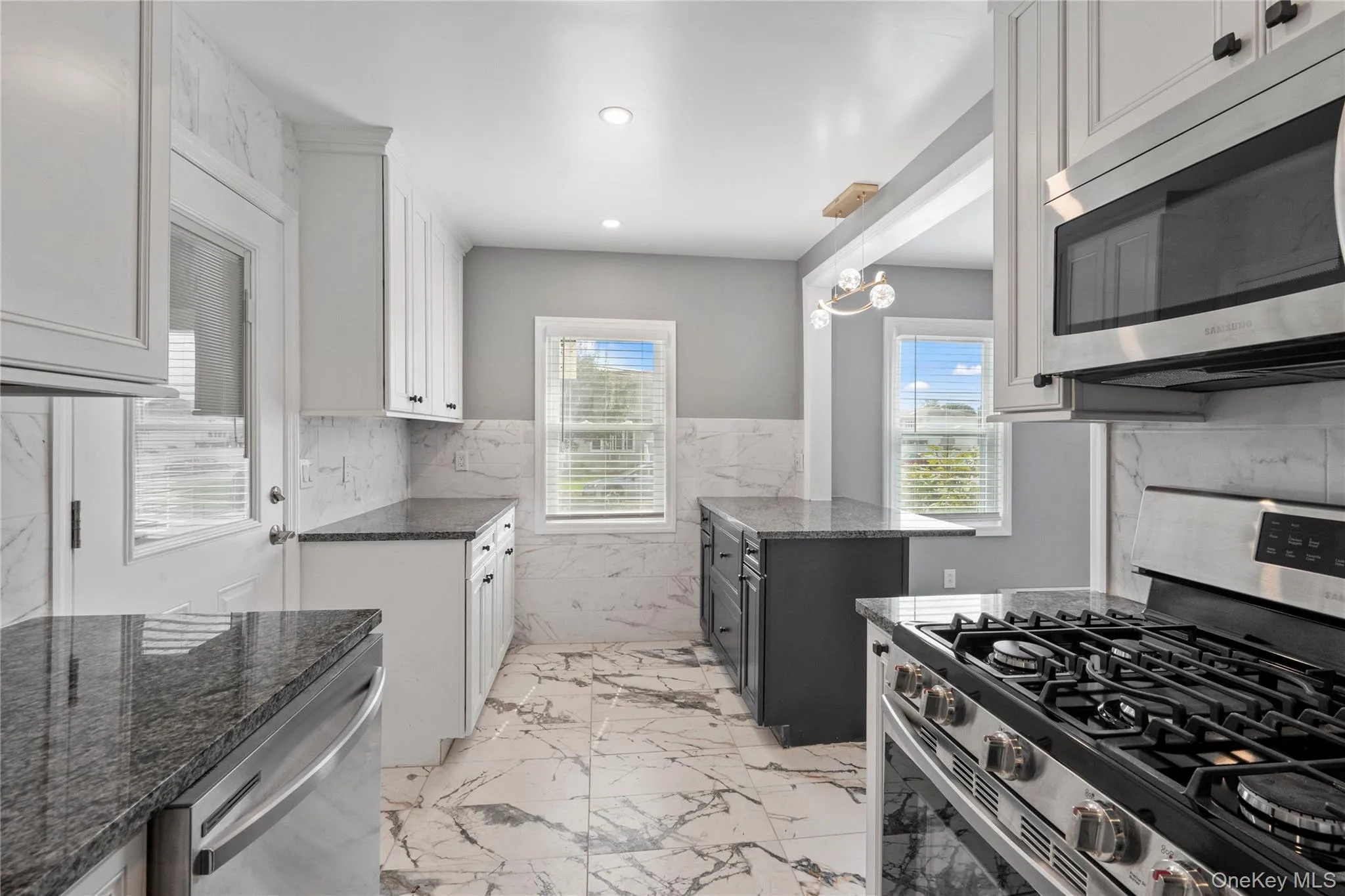 Kitchen with appliances with stainless steel finishes, dark stone countertops, white cabinetry, light marble finish floors, and recessed lighting Kitchen with appliances with stainless steel finishes, dark stone countertops, white cabinetry, light marble finish floors, and recessed lighting