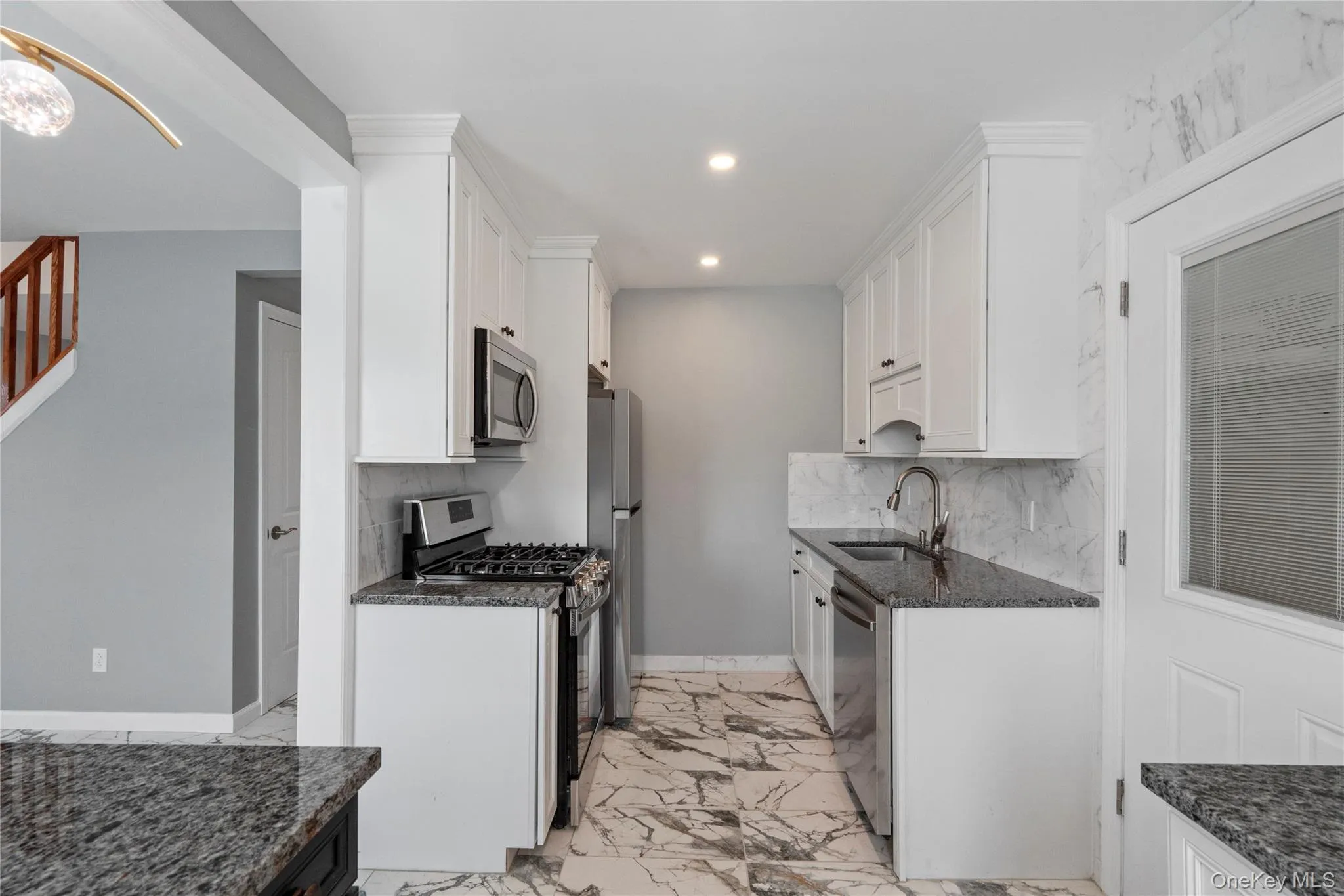 Kitchen featuring stainless steel appliances, dark stone counters, white cabinets, light marble finish floors, and recessed lighting Kitchen featuring stainless steel appliances, dark stone counters, white cabinets, light marble finish floors, and recessed lighting