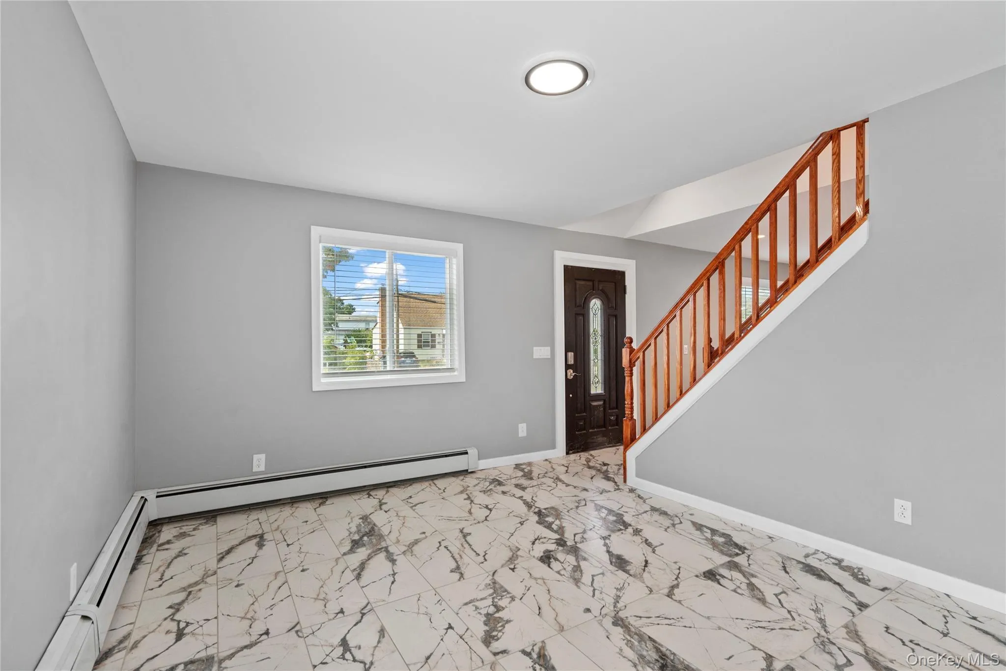 Foyer entrance with stairs, light marble finish floors, and a baseboard radiator Foyer entrance with stairs, light marble finish floors, and a baseboard radiator