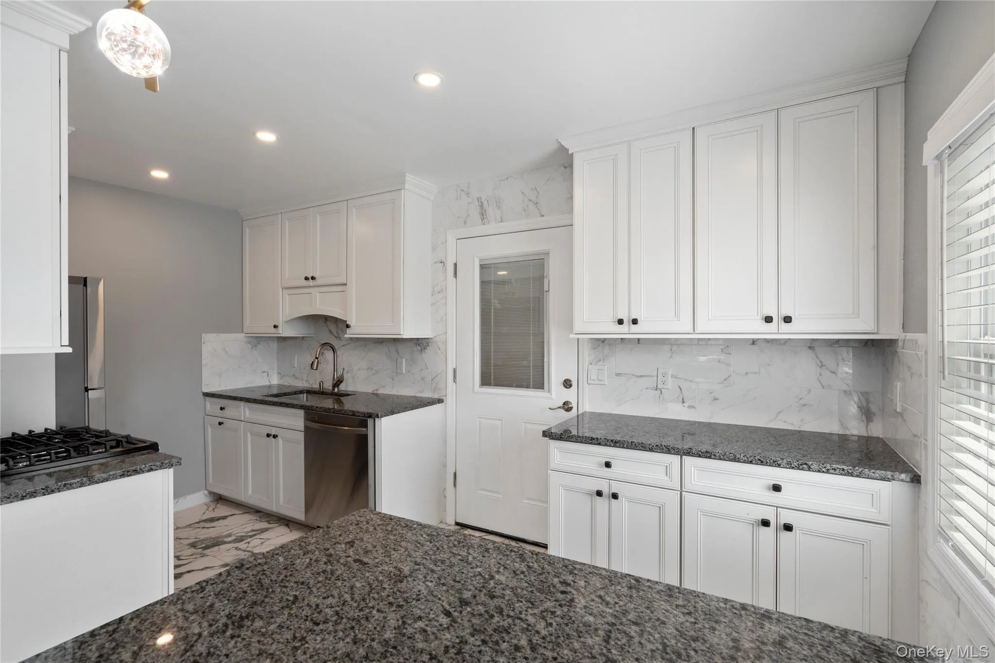 Kitchen with white cabinets, dark stone countertops, recessed lighting, backsplash, and stainless steel dishwasher Kitchen with white cabinets, dark stone countertops, recessed lighting, backsplash, and stainless steel dishwasher