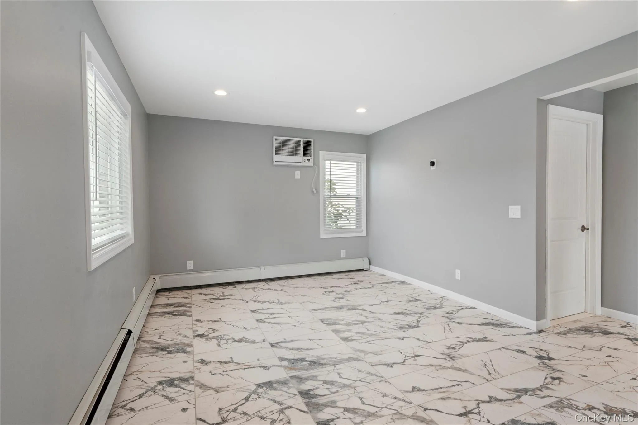 Unfurnished room featuring light marble finish flooring, recessed lighting, baseboard heating, and a wall mounted air conditioner Unfurnished room featuring light marble finish flooring, recessed lighting, baseboard heating, and a wall mounted air conditioner