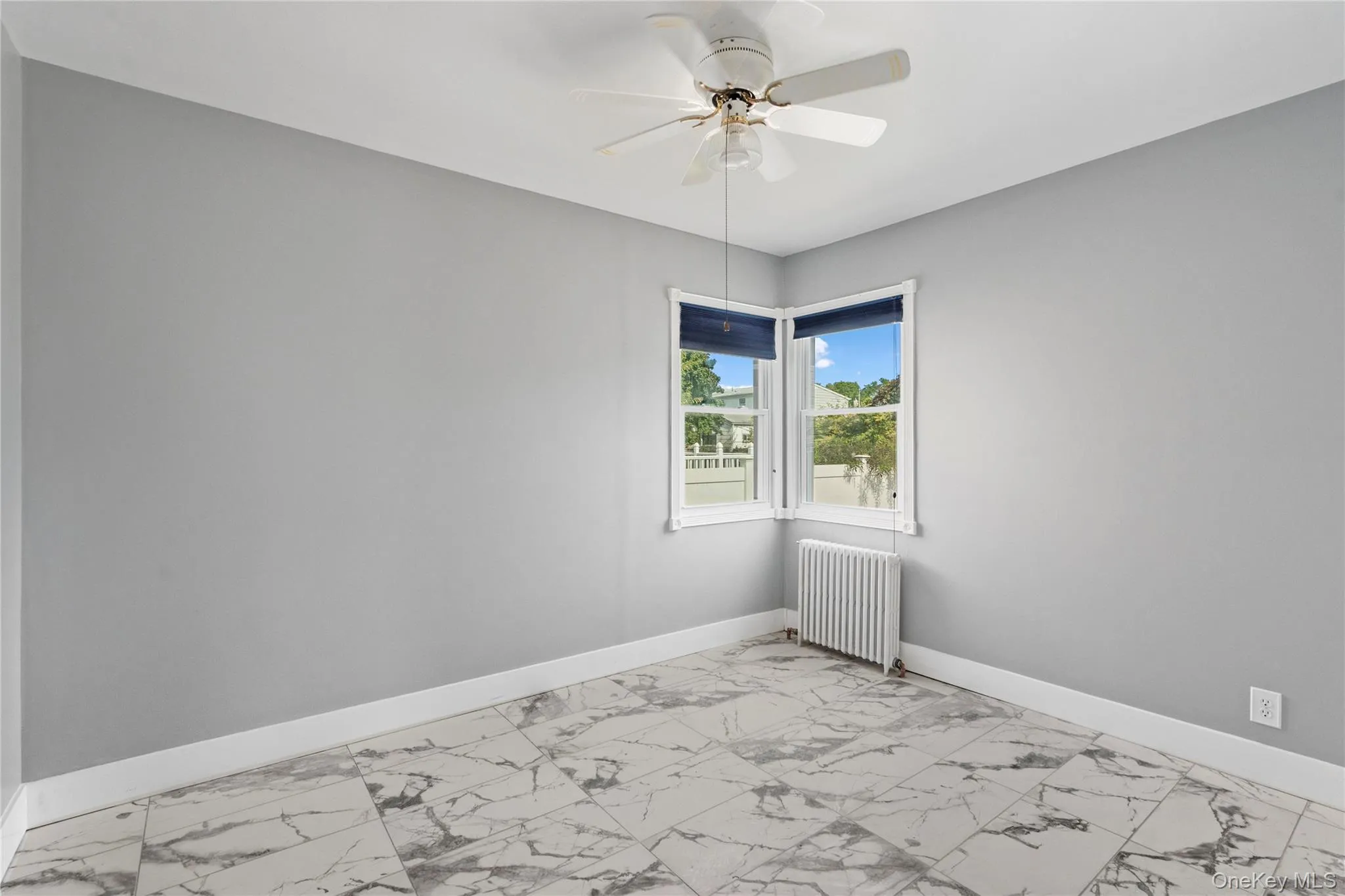 Spare room featuring light marble finish floors, radiator heating unit, and ceiling fan Spare room featuring light marble finish floors, radiator heating unit, and ceiling fan